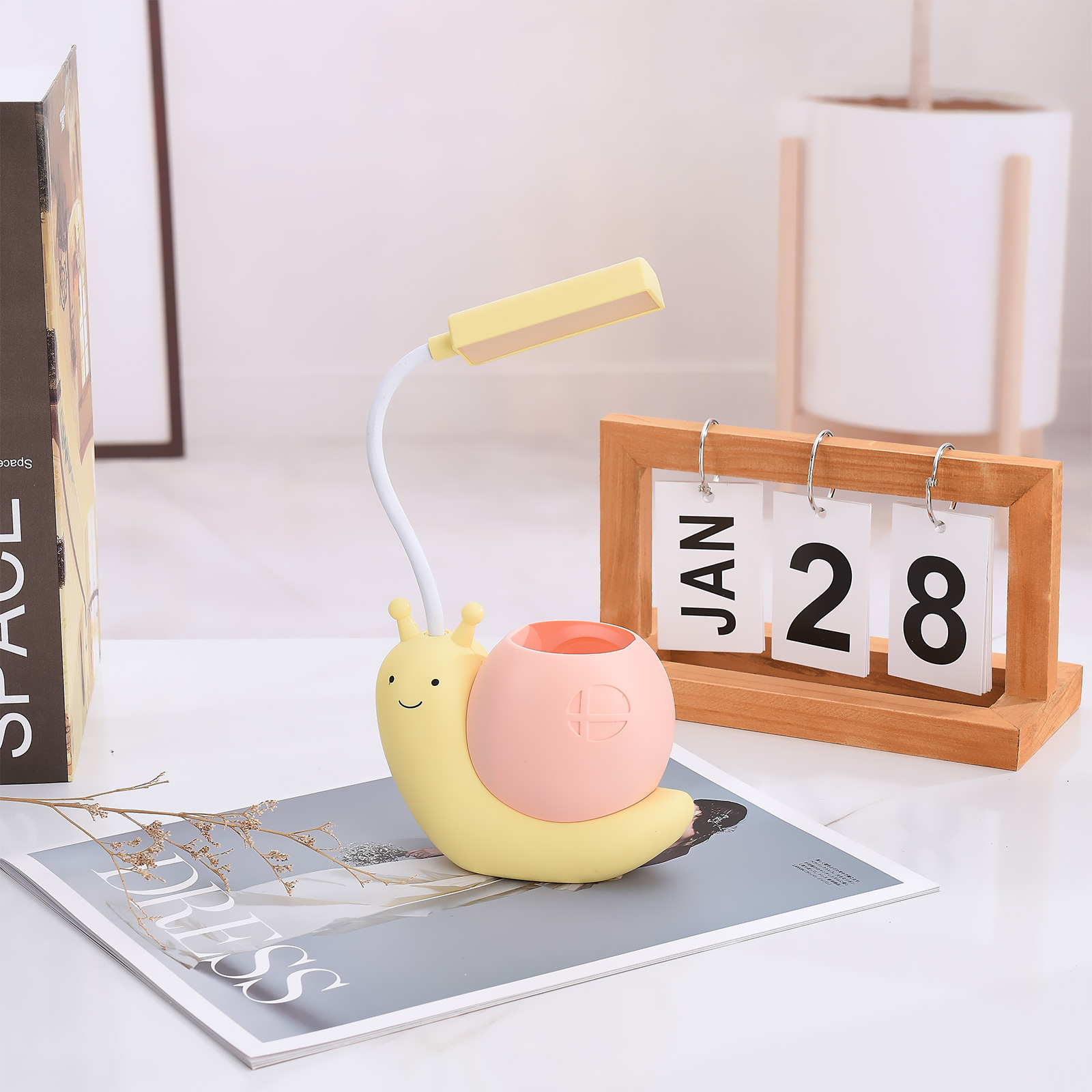 Eine gelbe, schneckenförmige Lampe mit rosa Schale, ein Kalender mit dem 28. Januar und eine Zeitschrift.