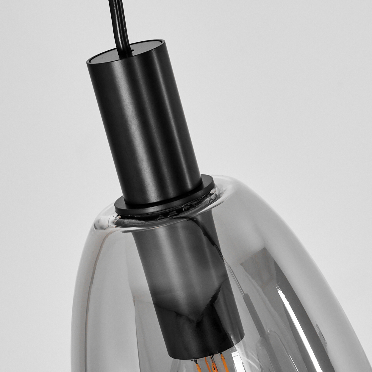 Eine moderne Pendelleuchte mit schwarzem zylindrischen Oberteil und einem klaren, tropfenförmigen Glasschirm. Die Glühfäden sind sichtbar.