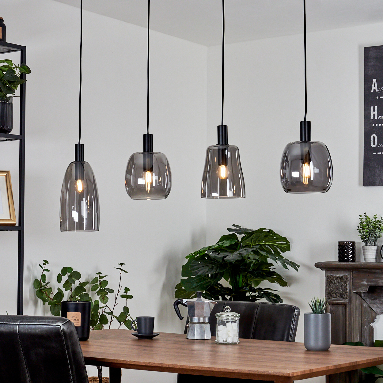 Vier graue Glas-Pendelleuchten über einem Holztisch. Pflanzen, Kaffeemaschine und andere Dekoration sind sichtbar.
