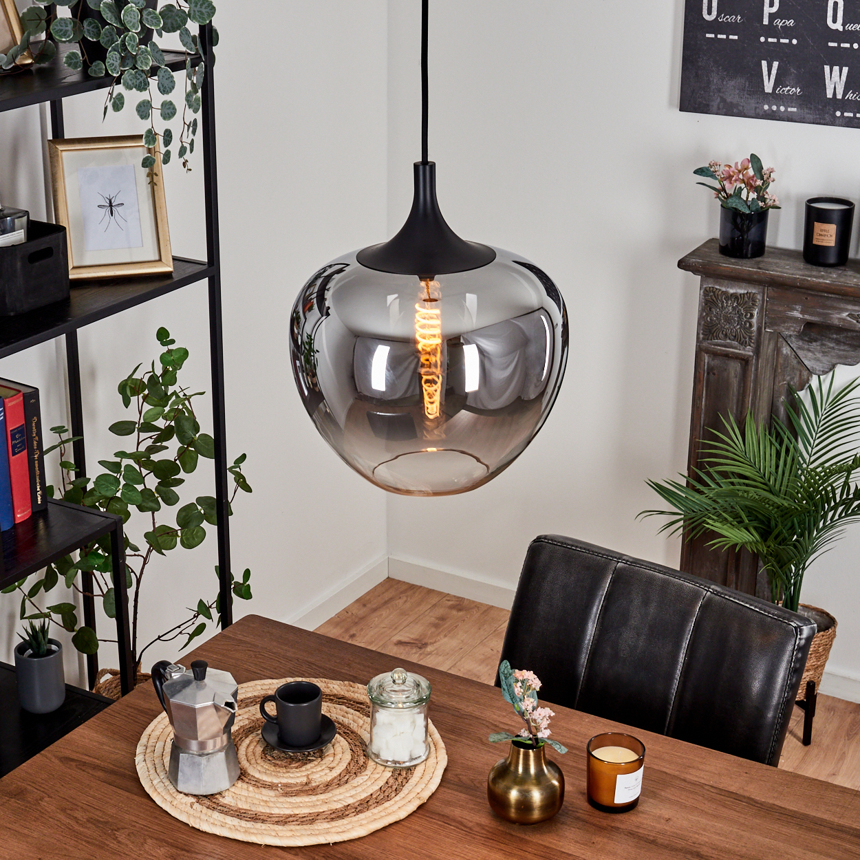 Ein modernes Esszimmer mit großer Glas-Hängelampe über einem Holztisch, Kaffeeset und Pflanzen.