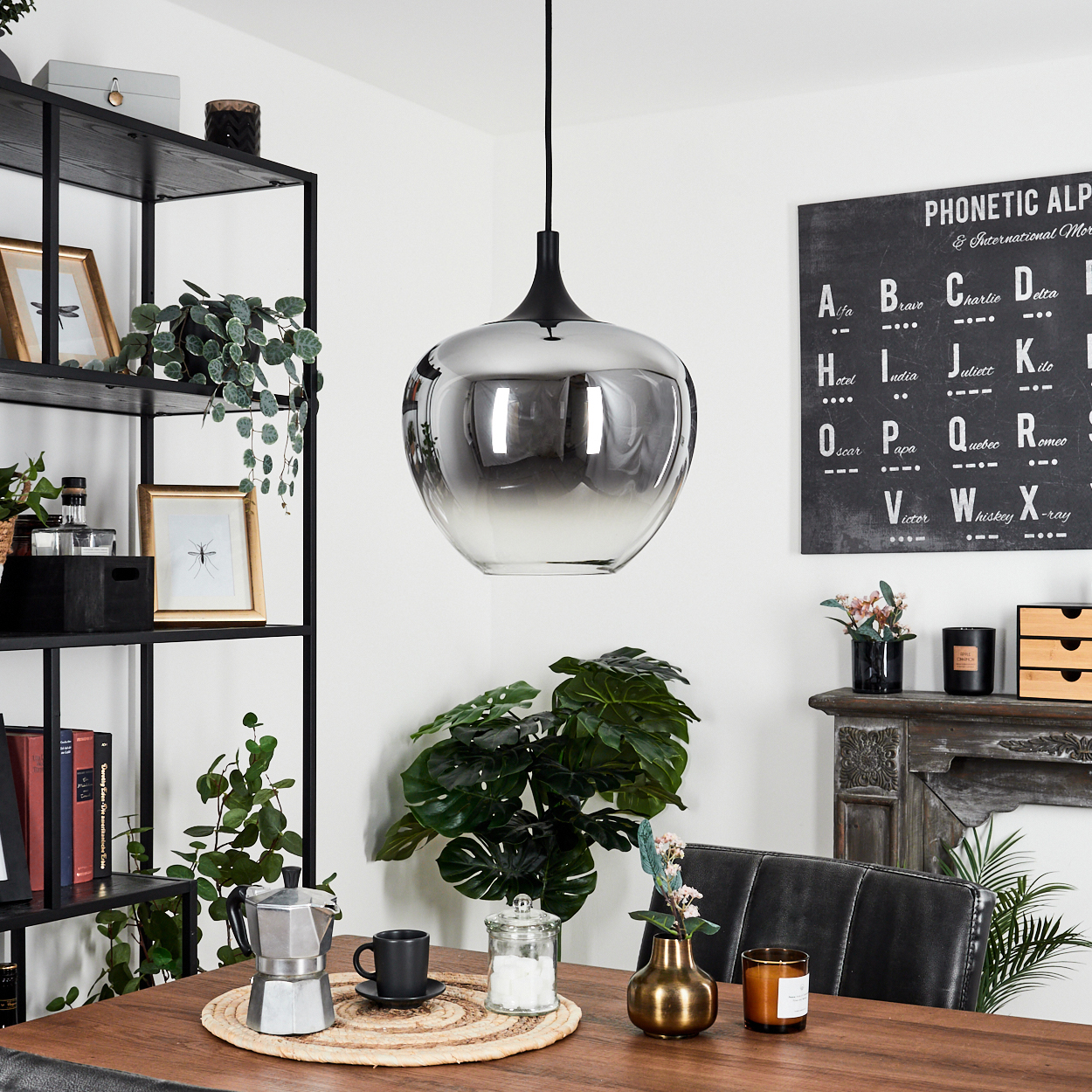 Ein modernes Esszimmer mit großer Leuchte, Holztisch und einer Tafel mit phonetischem Alphabet.