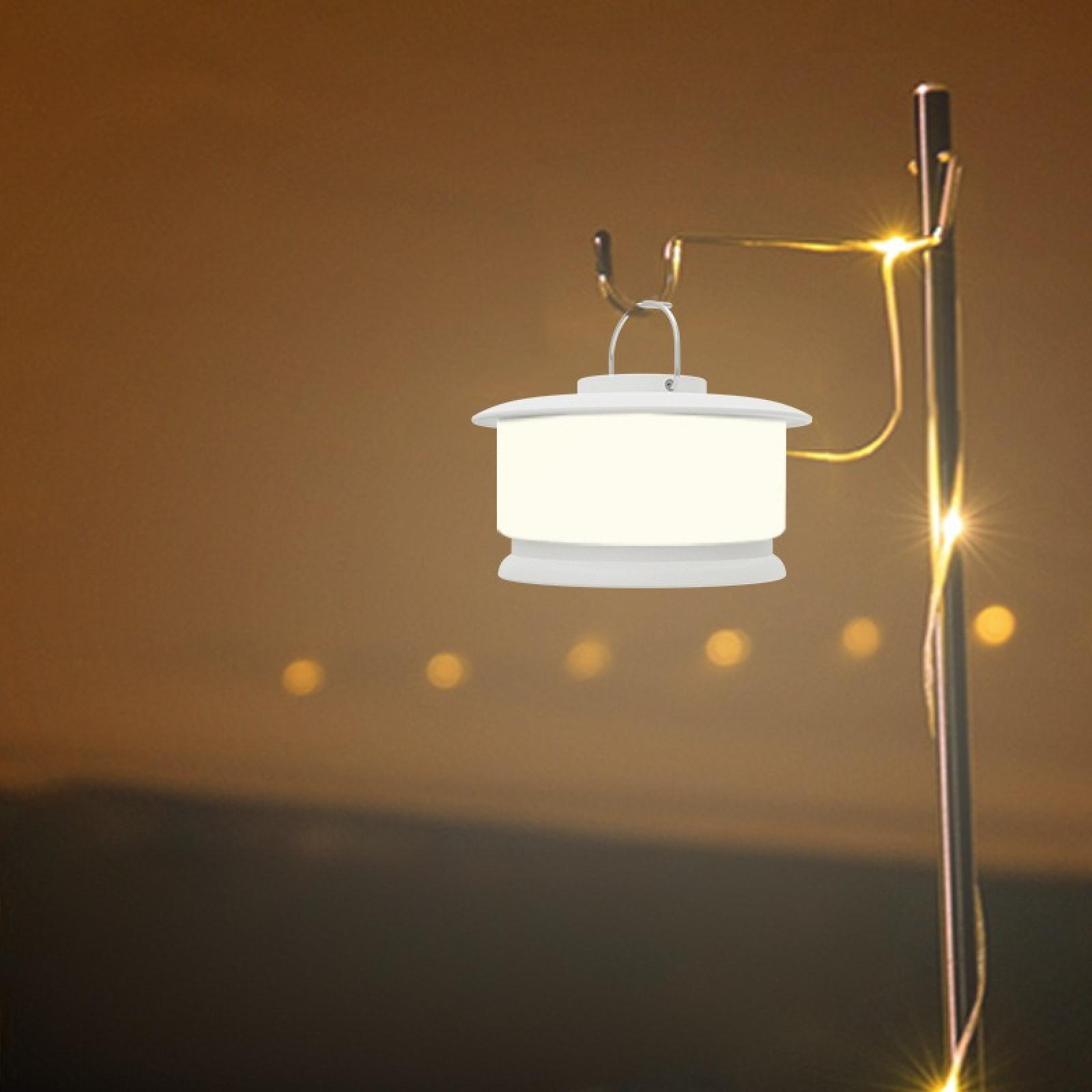 Eine weiße Laterne hängt an einem Metallpfahl. Lichter sind an. Der Hintergrund ist mit Orangetönen verschwommen.