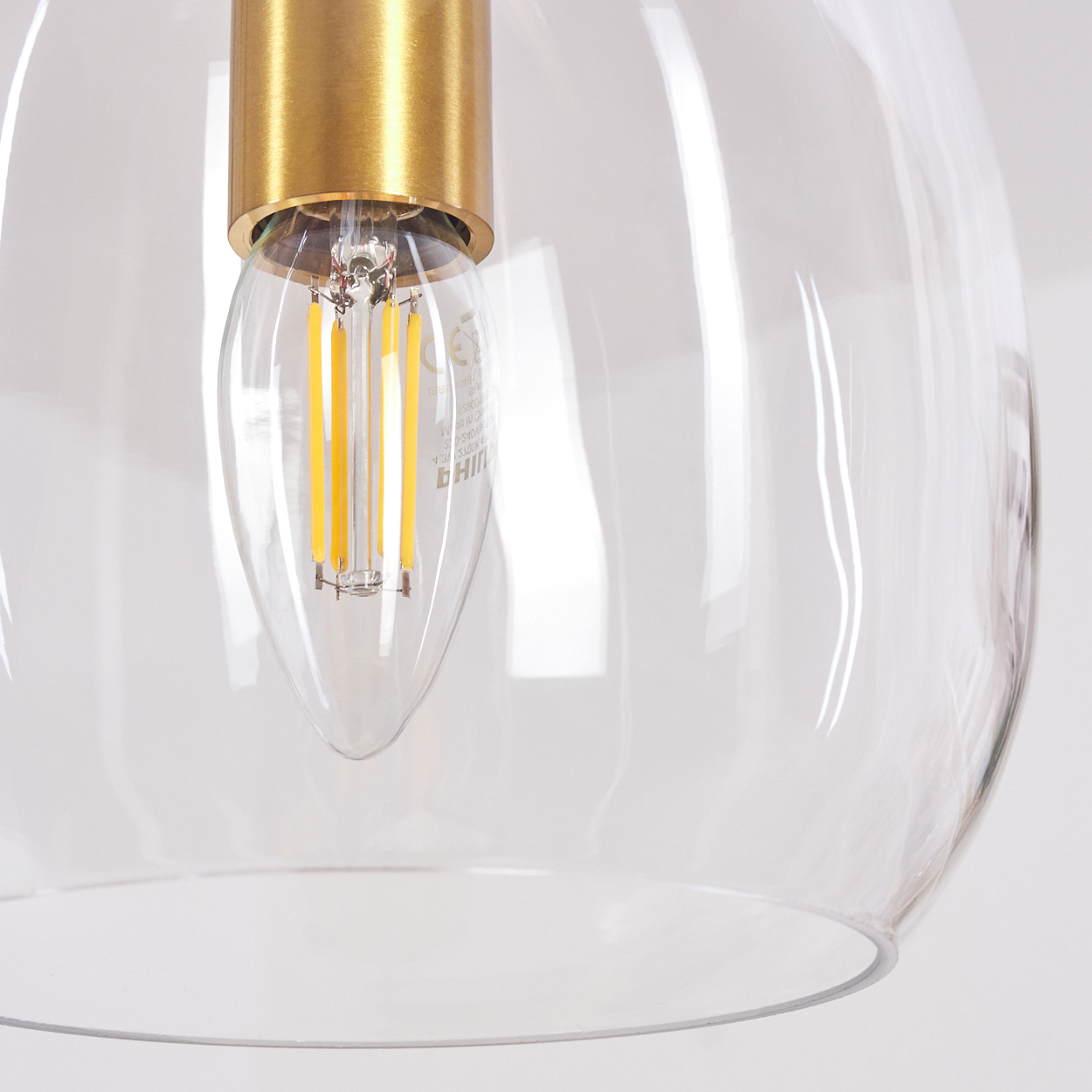 Nahaufnahme einer Leuchte. Eine klare Glaskugel umschließt eine gelb leuchtende LED-Glühbirne. Oben befindet sich eine goldfarbene Metallbefestigung.