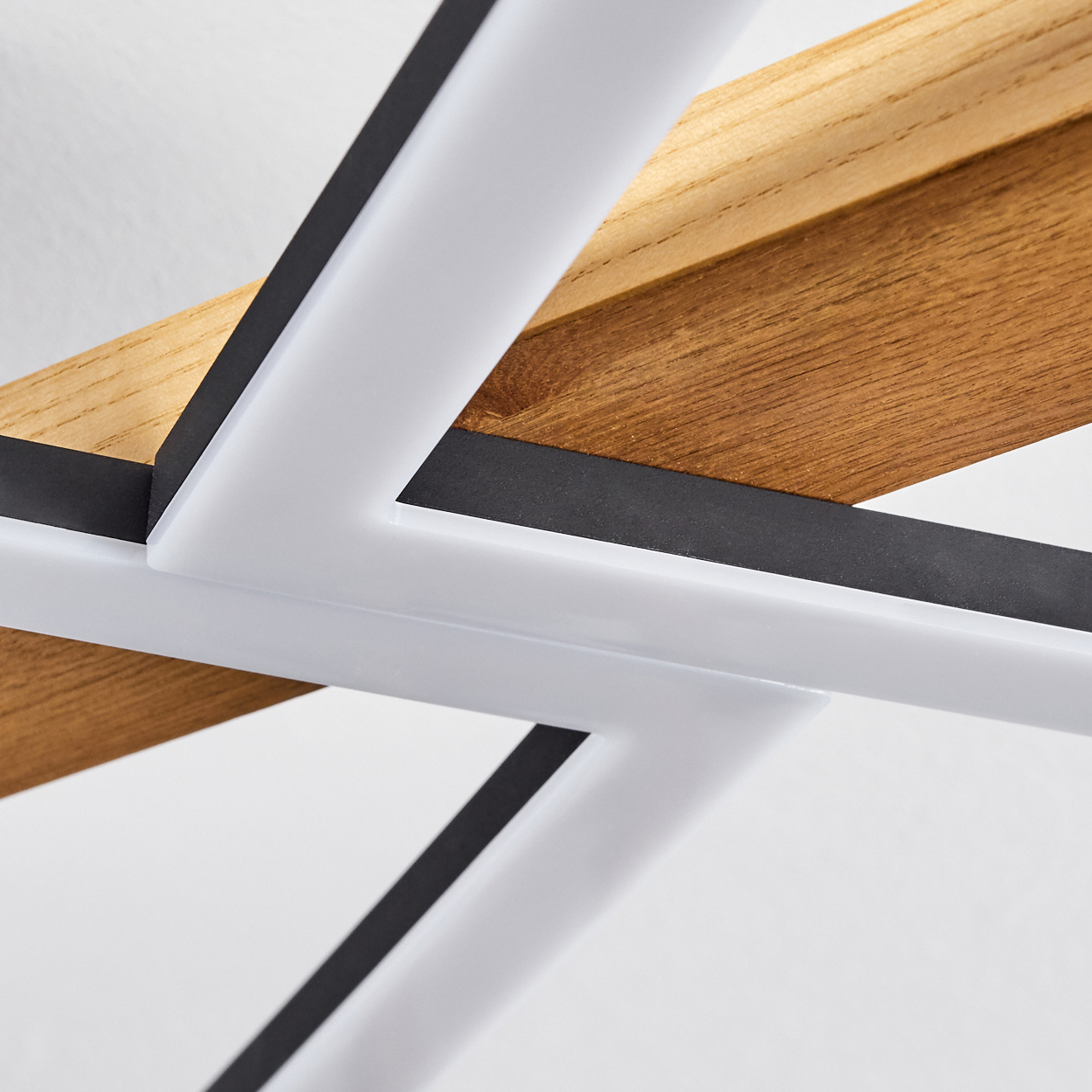 Nahaufnahme einer modernen Deckenleuchte. Merkmale: weiße geometrische Formen, schwarze Linien und Holzbalken vor weißem Hintergrund.