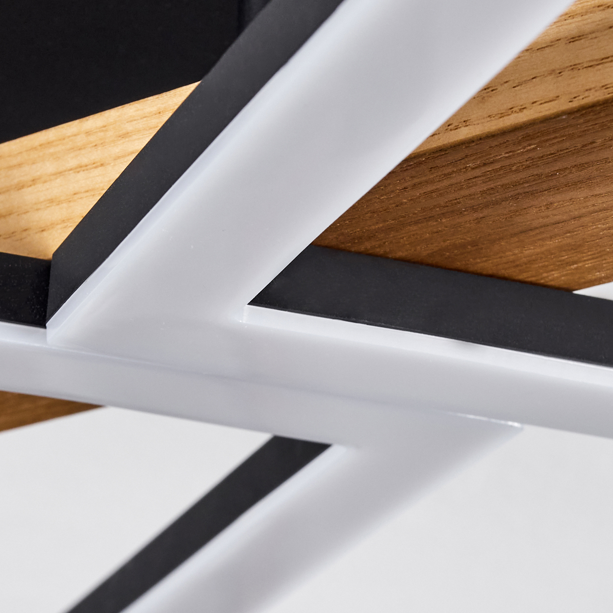 Nahaufnahme einer Deckenleuchte mit weißen, schwarzen und holzfarbenen Elementen. Das Design weist geometrische Formen auf.