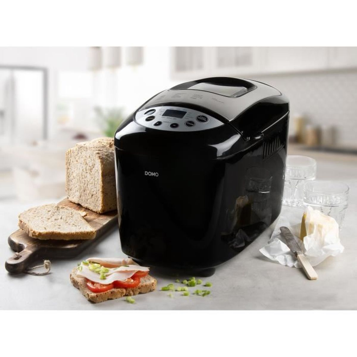 Ein schwarzer Brotbackautomat mit Brot, Toast und einem Sandwich. Butter und ein Messer liegen daneben. Im Hintergrund sind zwei Gläser.