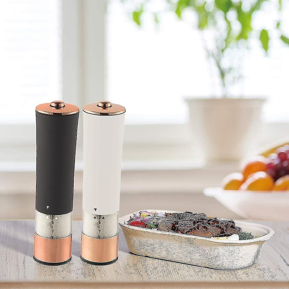 Zwei elektrische Salz- und Pfeffermühlen, ein Gericht mit Essen und eine Schüssel mit Obst stehen auf einem Tisch. Im Hintergrund ist ein Fenster.