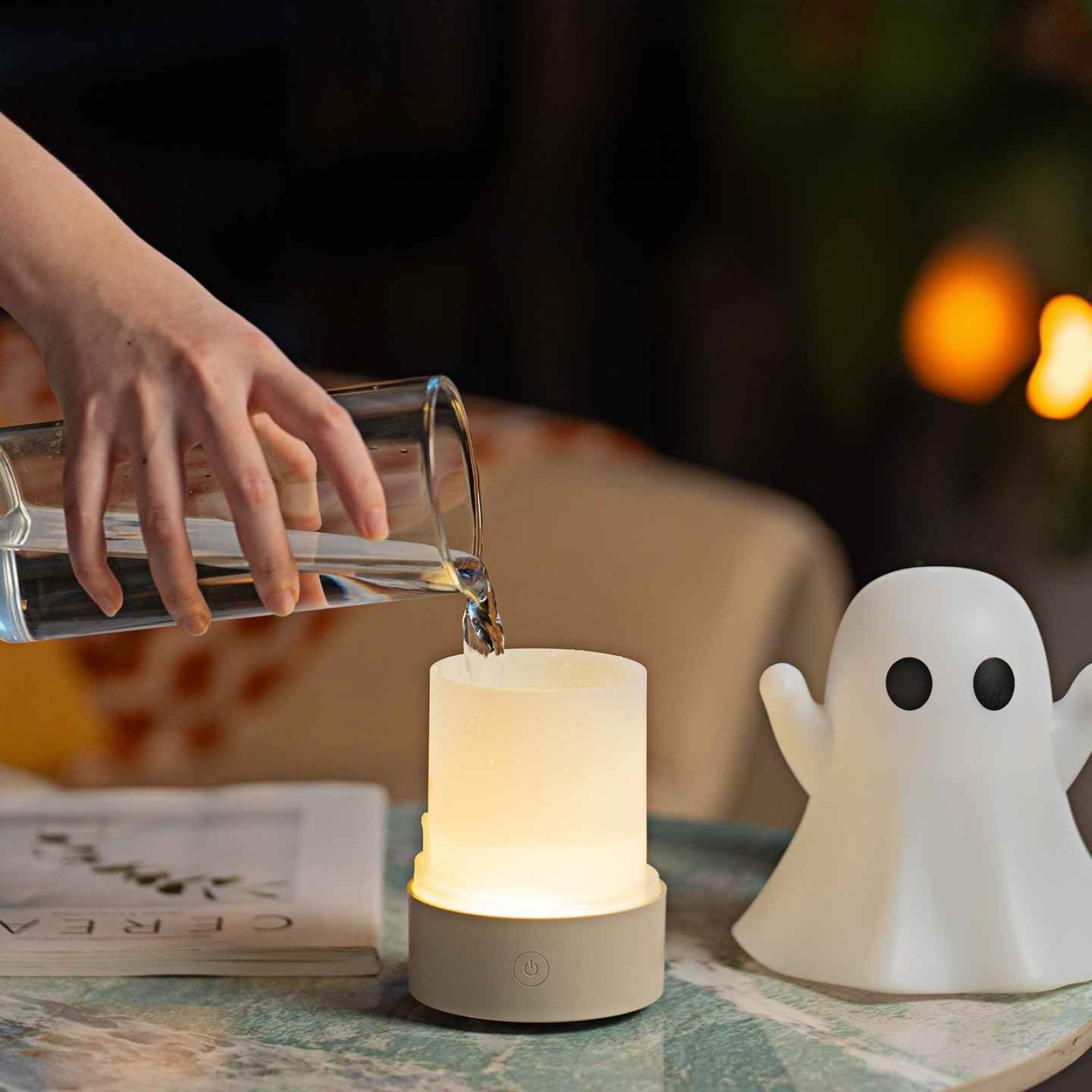 Eine Hand gießt Wasser in eine leuchtende kerzenförmige Lampe. Daneben steht ein weißes, geisterförmiges Licht.