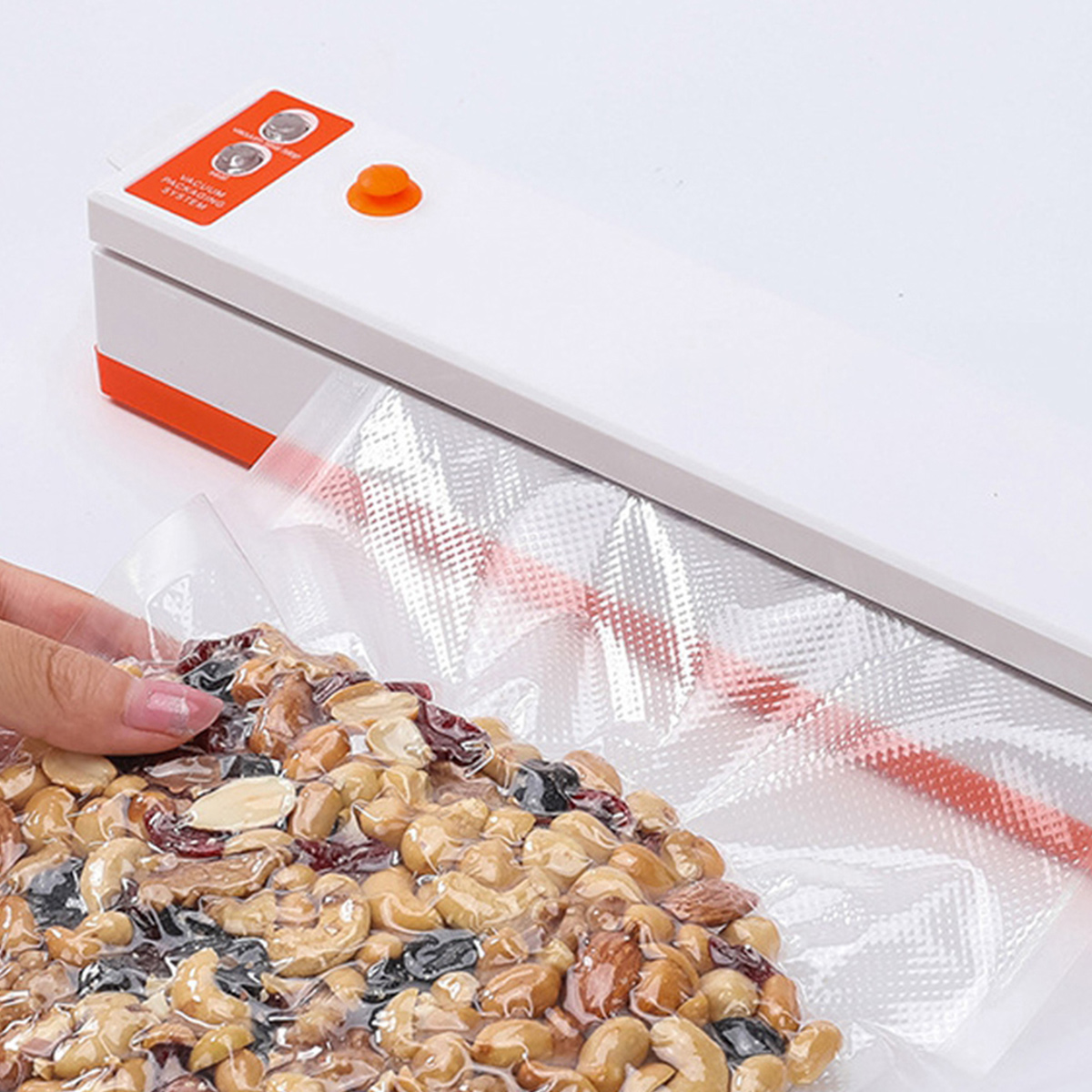 Eine Hand versiegelt eine Tüte mit gemischten Nüssen mit einem Vakuumierer. Das Siegelgerät ist weiß und orange. Nüsse sind in einem durchsichtigen Plastikbeutel.