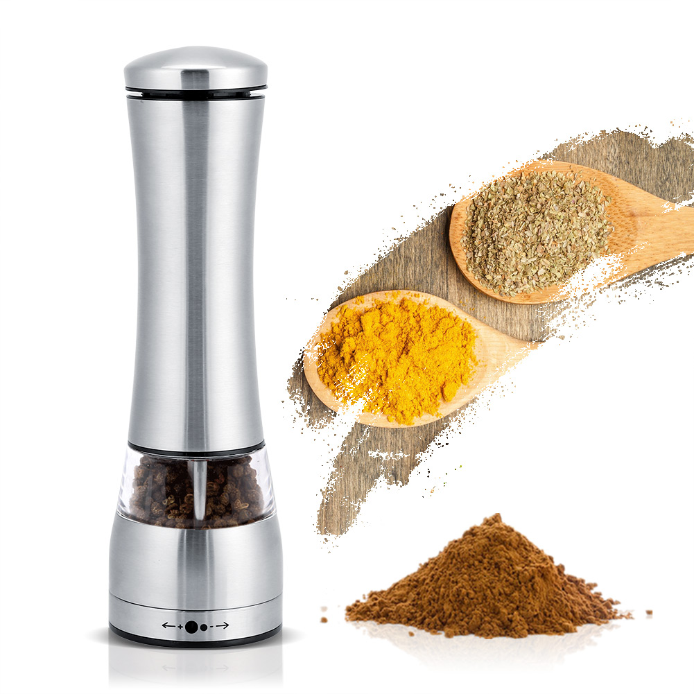 Eine silberne Pfeffermühle mit schwarzen Pfefferkörnern, zwei Holzlöffel mit Kräutern und ein Haufen brauner Gewürze auf weißem Hintergrund.