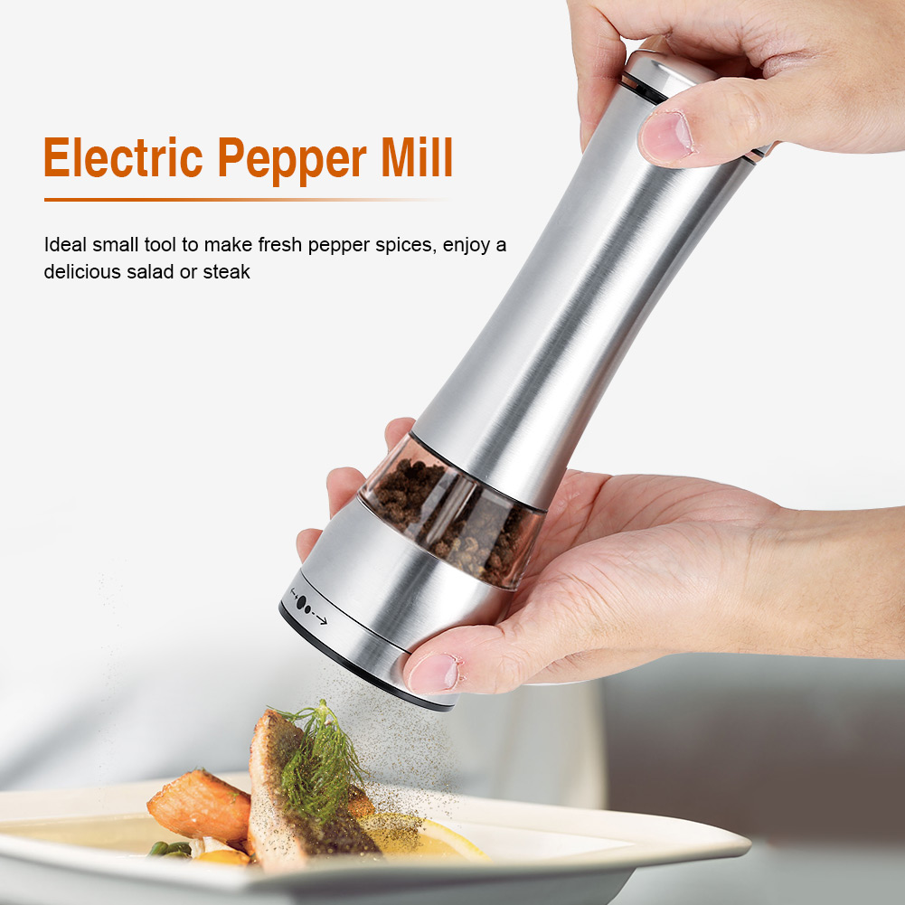 Eine Hand hält eine silberne elektrische Pfeffermühle und mahlt Pfeffer auf einen Teller mit Essen. Das Essen beinhaltet Fisch und Zitrone.
