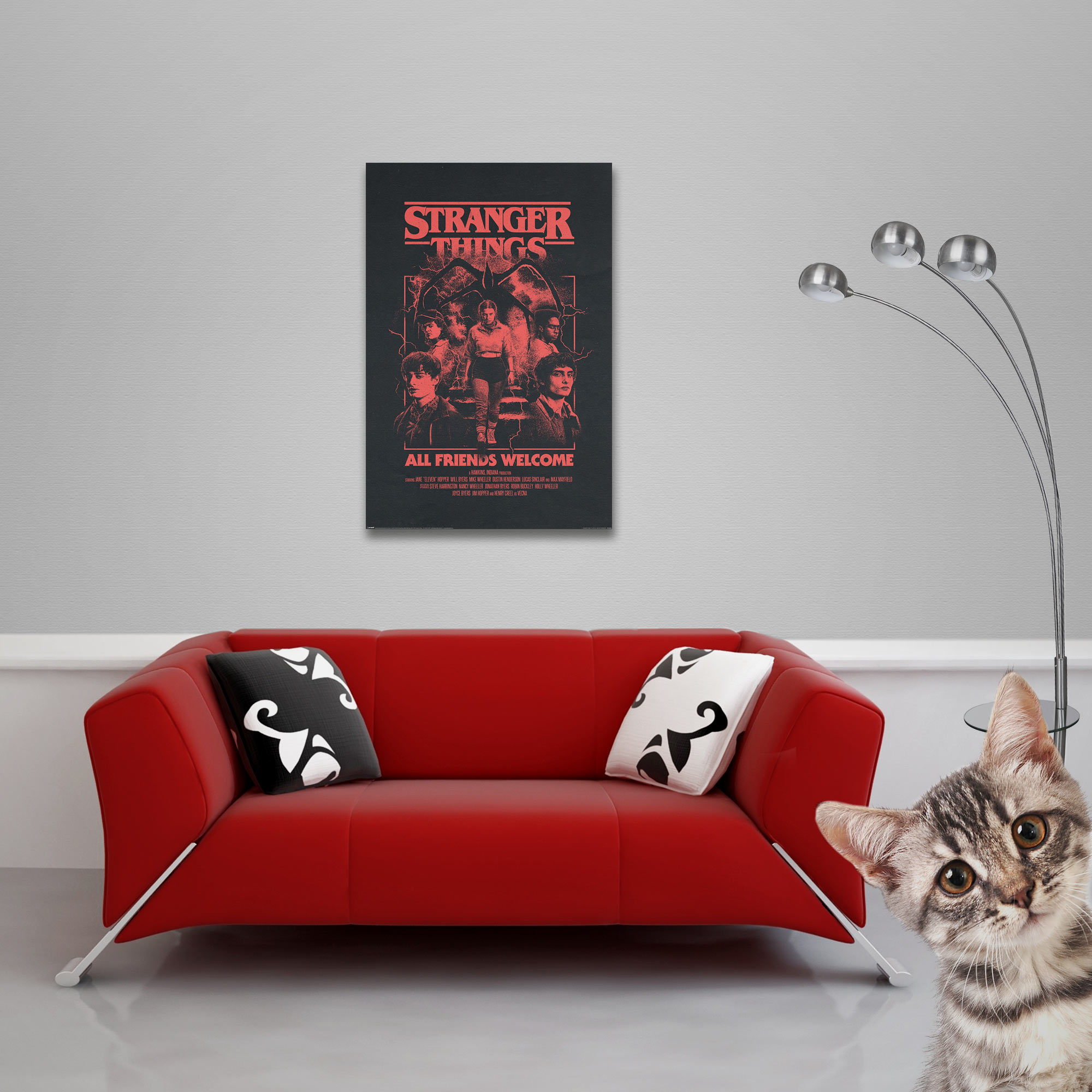 Rotes Sofa mit Kissen unter einem 'Stranger Things'-Poster. Eine Katze schaut von rechts herein. Rechts ist eine Lampe.