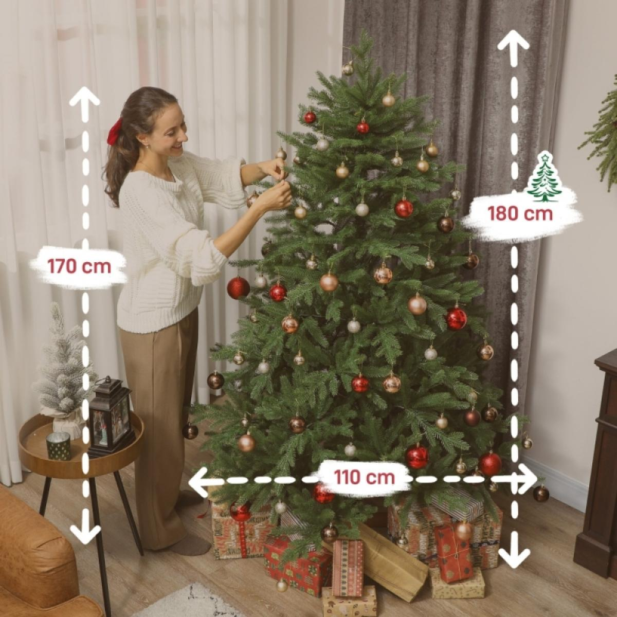 Frau schmückt einen Weihnachtsbaum mit Ornamenten. Der Baum ist mit roten, goldenen und silbernen Kugeln geschmückt. Geschenke liegen unter dem Baum.