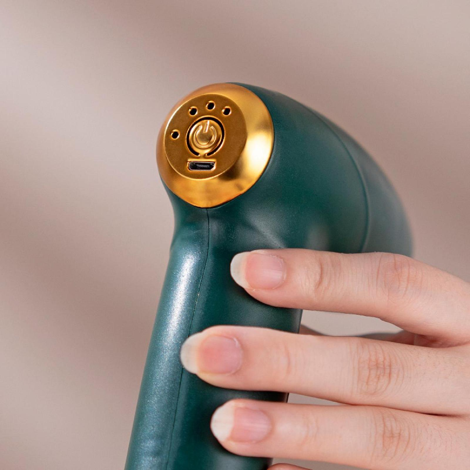 Eine Hand, die ein grün-goldenes Gerät mit einem Ein-/Ausschalter hält. Der Hintergrund ist neutral.