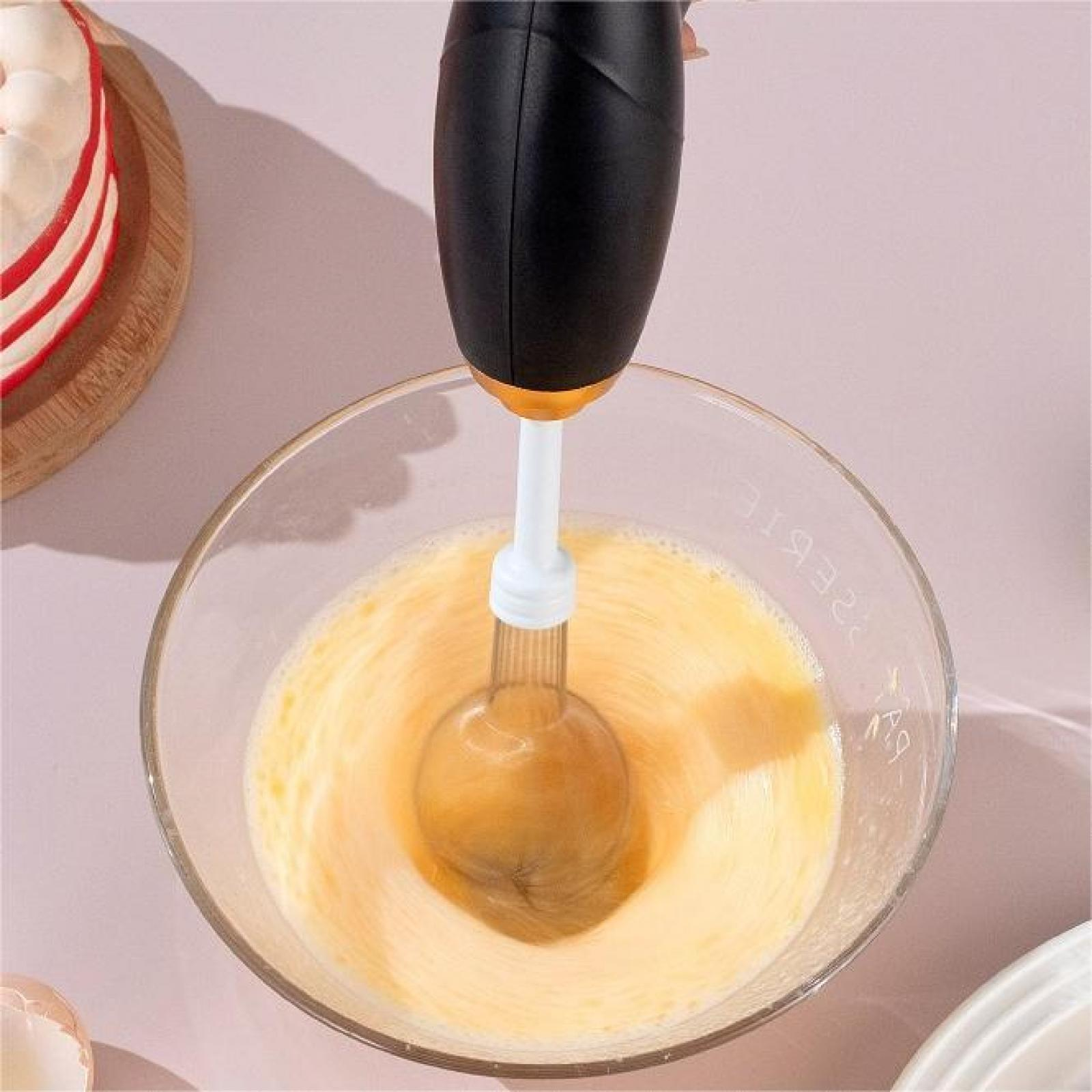 Ein Handmixer in einer Schüssel mit Eiern. Kuchen auf einem Holzbrett im Hintergrund. Rosa Oberfläche.
