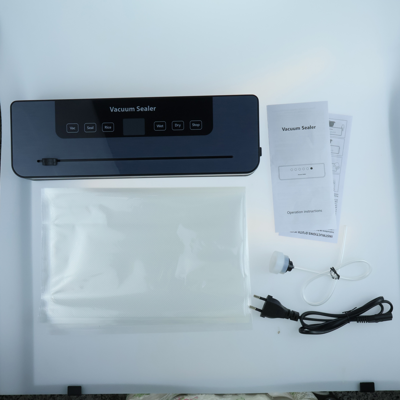 Vakuumiergerät-Set auf weißer Oberfläche. Enthält Gerät, Beutel, Anweisungen und Zubehör wie Pumpe und Netzkabel.