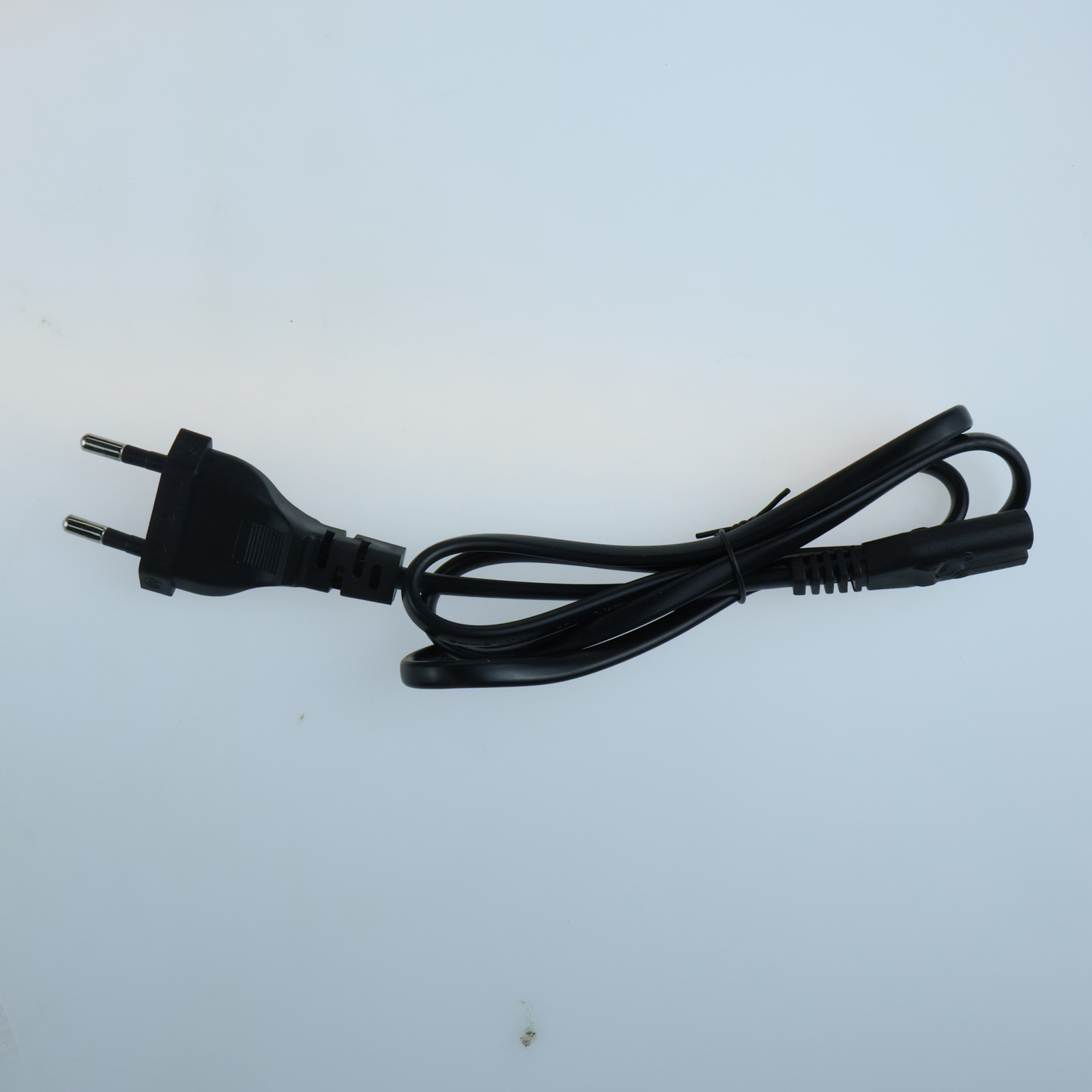 Ein schwarzes Netzkabel mit europäischem Stecker liegt auf einer weißen Oberfläche. Das Kabel ist gebogen und gewickelt.