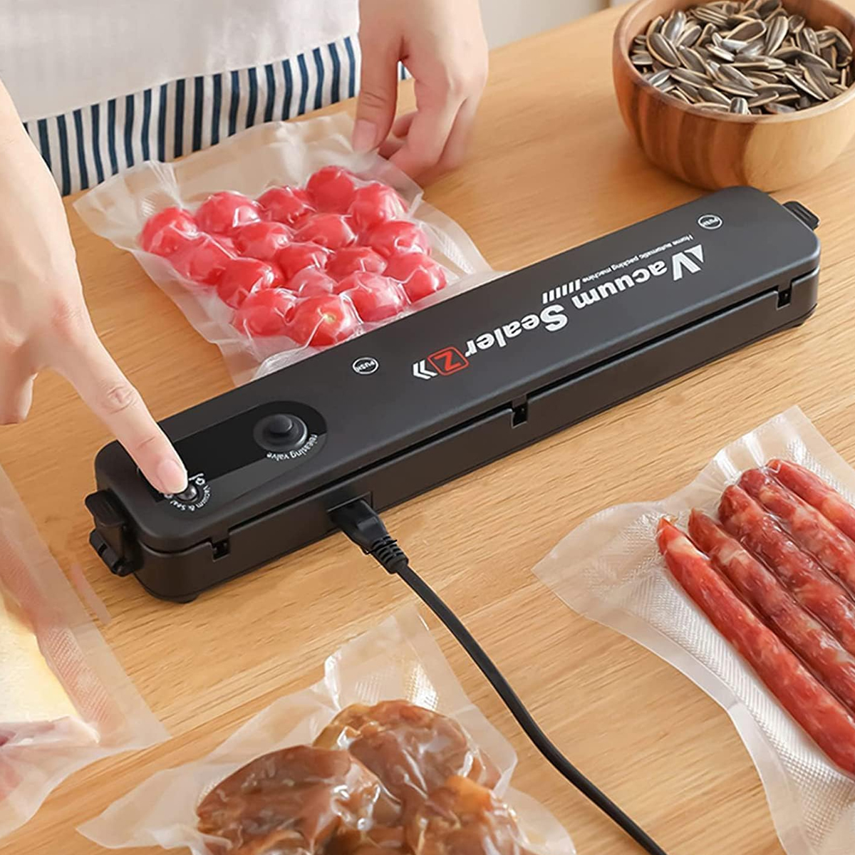 Eine Person benutzt ein Vakuumiergerät mit Lebensmitteln wie Tomaten und Würstchen. Eine Schüssel mit Sonnenblumenkernen ist im Hintergrund.