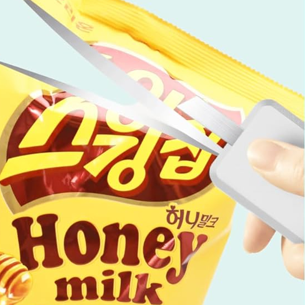 Schere schneidet eine gelbe Honey Milk Snack-Tüte. Hand hält die Schere. Auf der Tüte steht koreanischer Text und die Worte 'Honey Milk'.