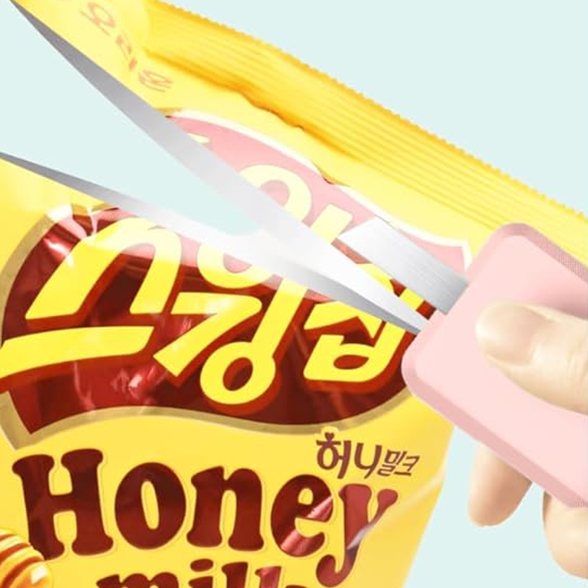 Eine Schere schneidet eine gelbe Honig-Milch-Snack-Tüte auf. Ein rosa Griff ist sichtbar. Die Tüte hat koreanischen Text.