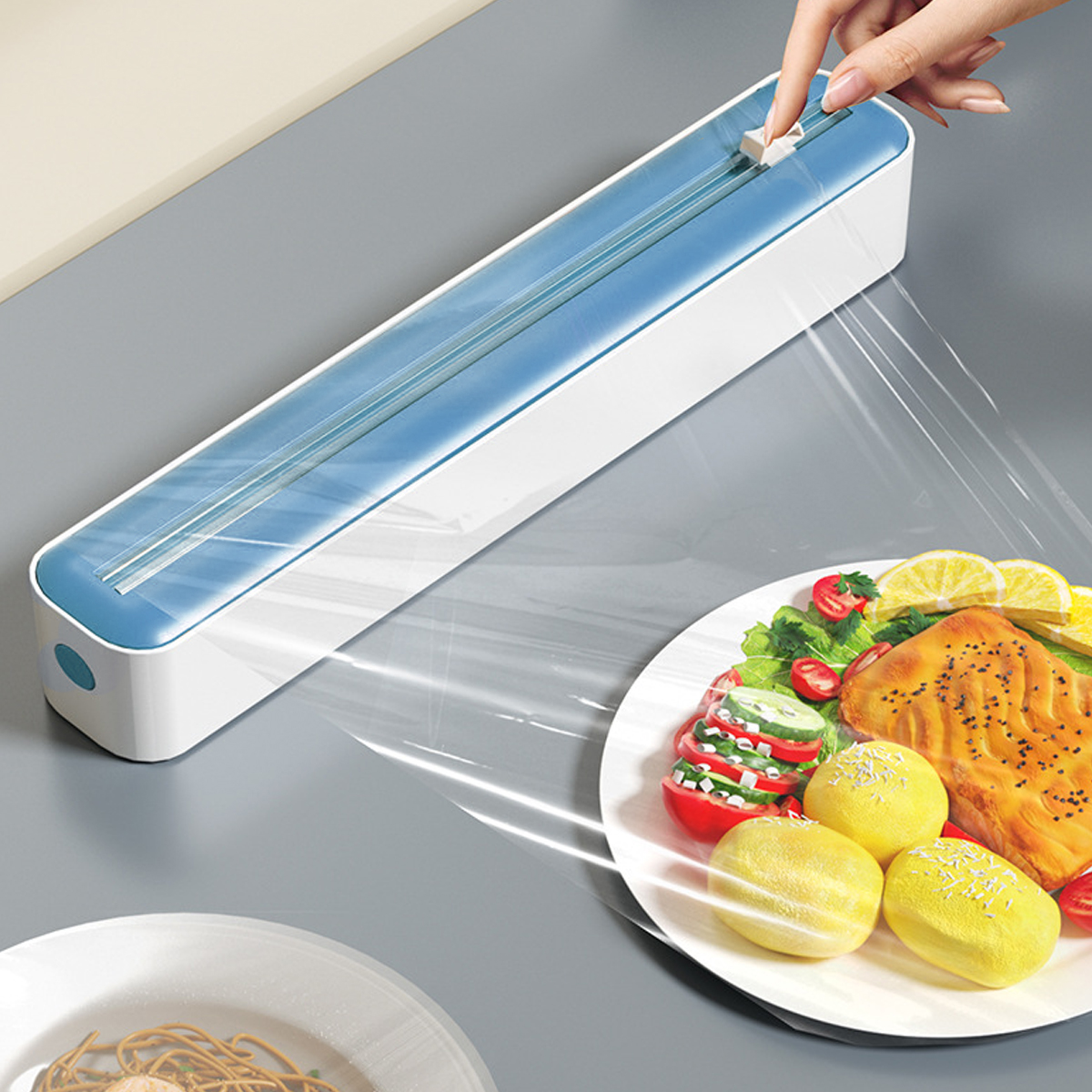 Eine Hand, die Plastikfolie über einen Teller mit Essen abgibt. Ein Behälter für die Folie befindet sich im Hintergrund.