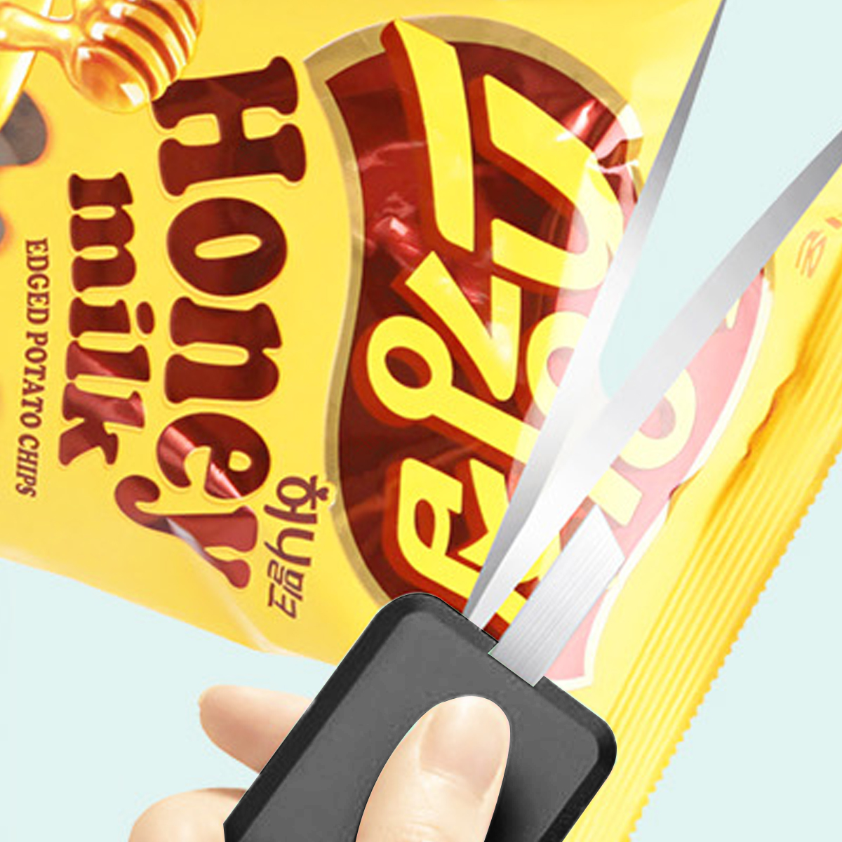 Schere schneidet eine Honig-Milch-Kartoffelchipstüte. Die Tüte ist gelb mit rotem Text. Eine Hand hält die Schere.