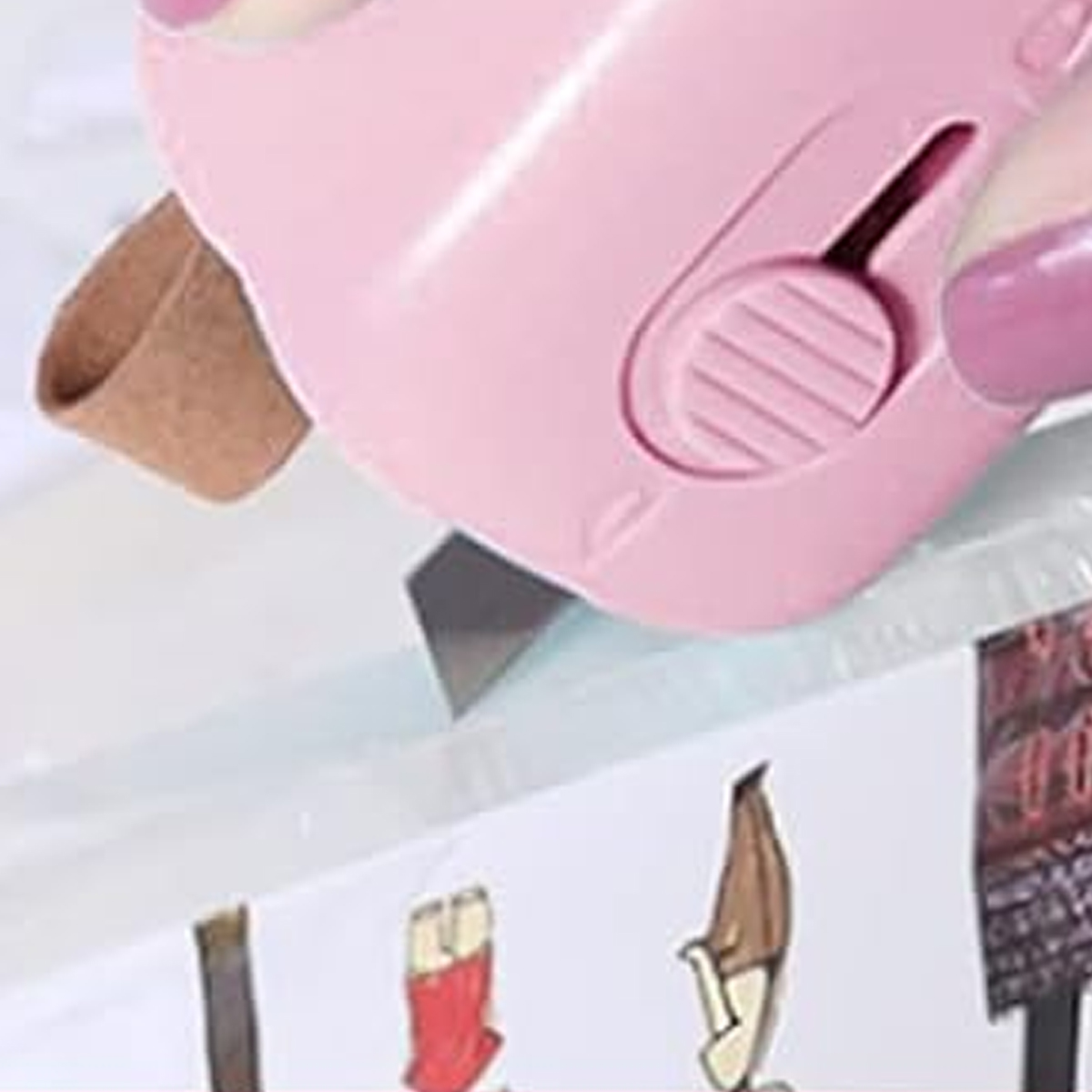 Ein rosa Kartonschneider schneidet eine weiße Oberfläche. Ein brauner Riemen ist am Schneider befestigt. Zeichnungen sind unten sichtbar.