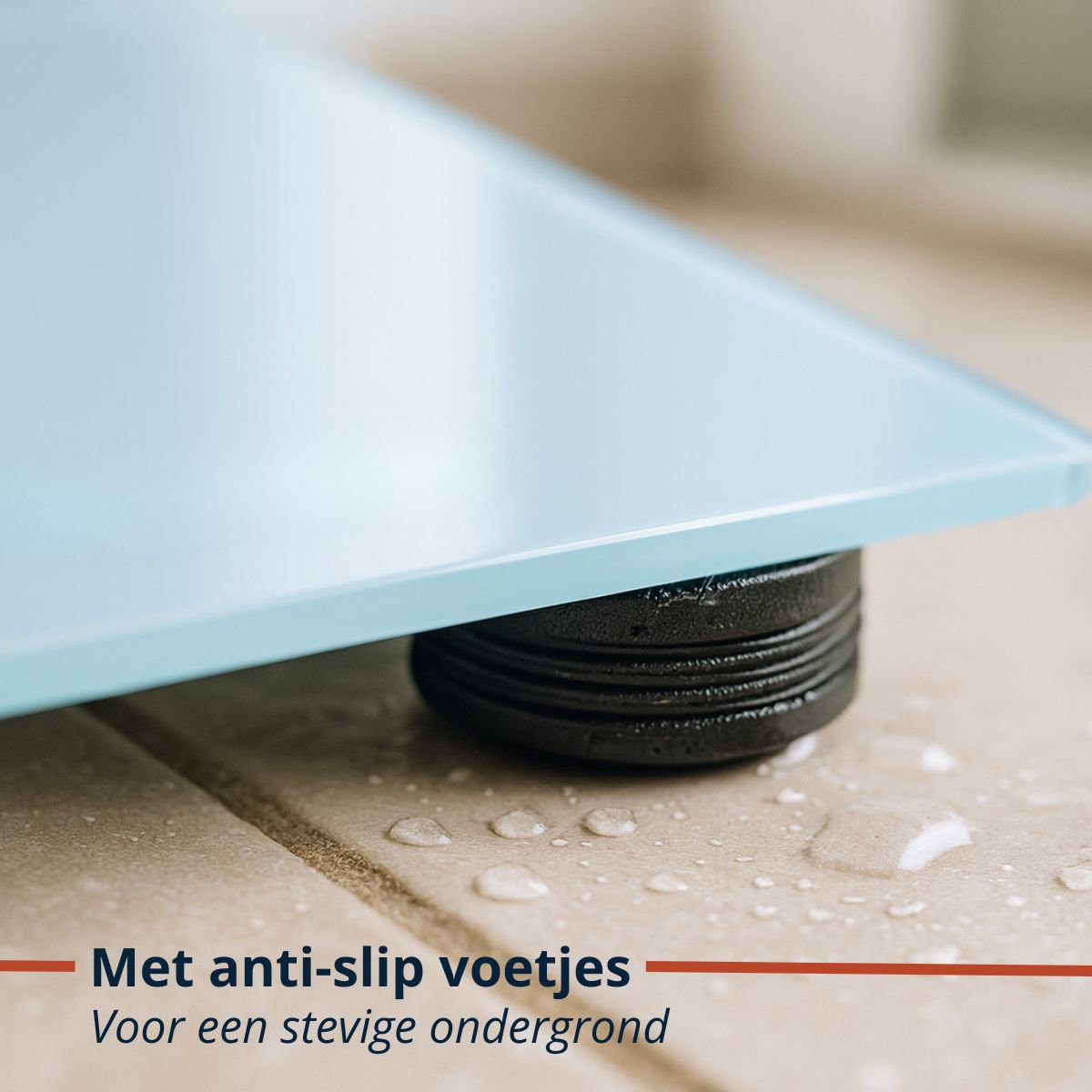 Close-up van een blauwe glazen weegschaal op een betegelde vloer. Zwarte basis met antislipvoetjes. Waterdruppels zichtbaar.