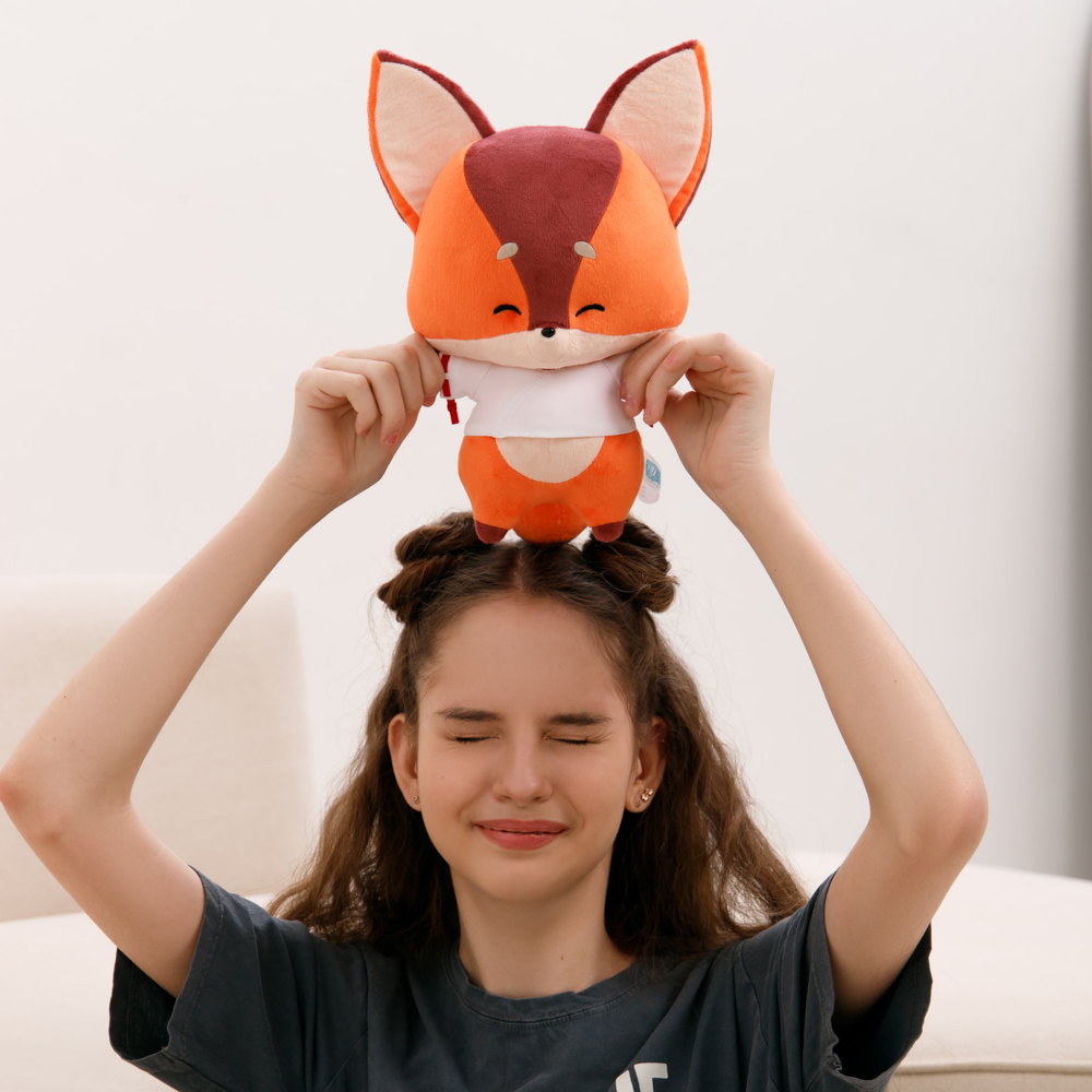 Ein Mädchen hält ein Fuchsplüschtier über ihrem Kopf. Das Plüschtier ist orange und braun. Das Mädchen lächelt mit geschlossenen Augen. Weißer Hintergrund.