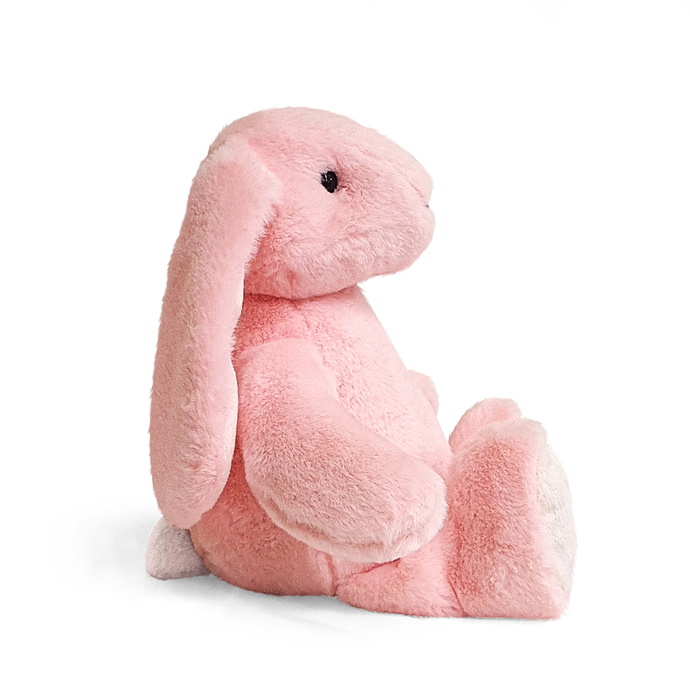 Ein rosa Plüschhase sitzt auf weißem Hintergrund. Er hat lange Ohren, einen flauschigen Körper und schwarze Augen. Das Fell ist weich und strukturiert.