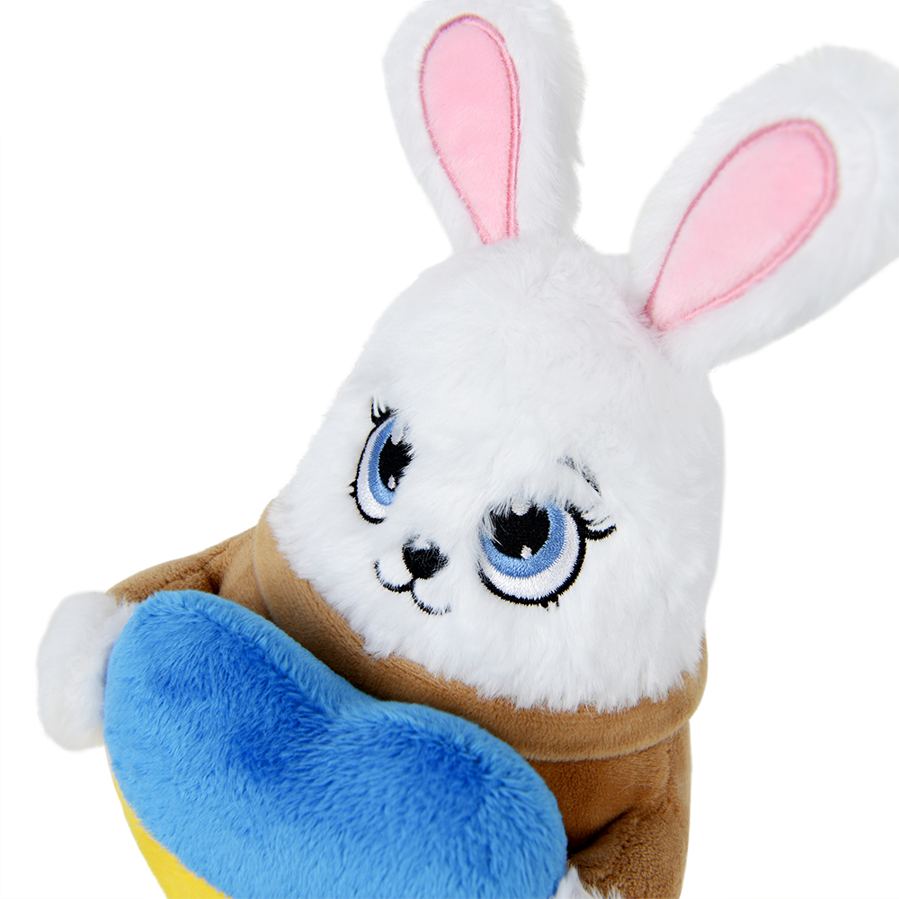 Ein weißes Plüschkaninchen mit rosa Ohren, blauen Augen und einer braunen Jacke, das ein blau-gelbes herzförmiges Plüschtier hält.