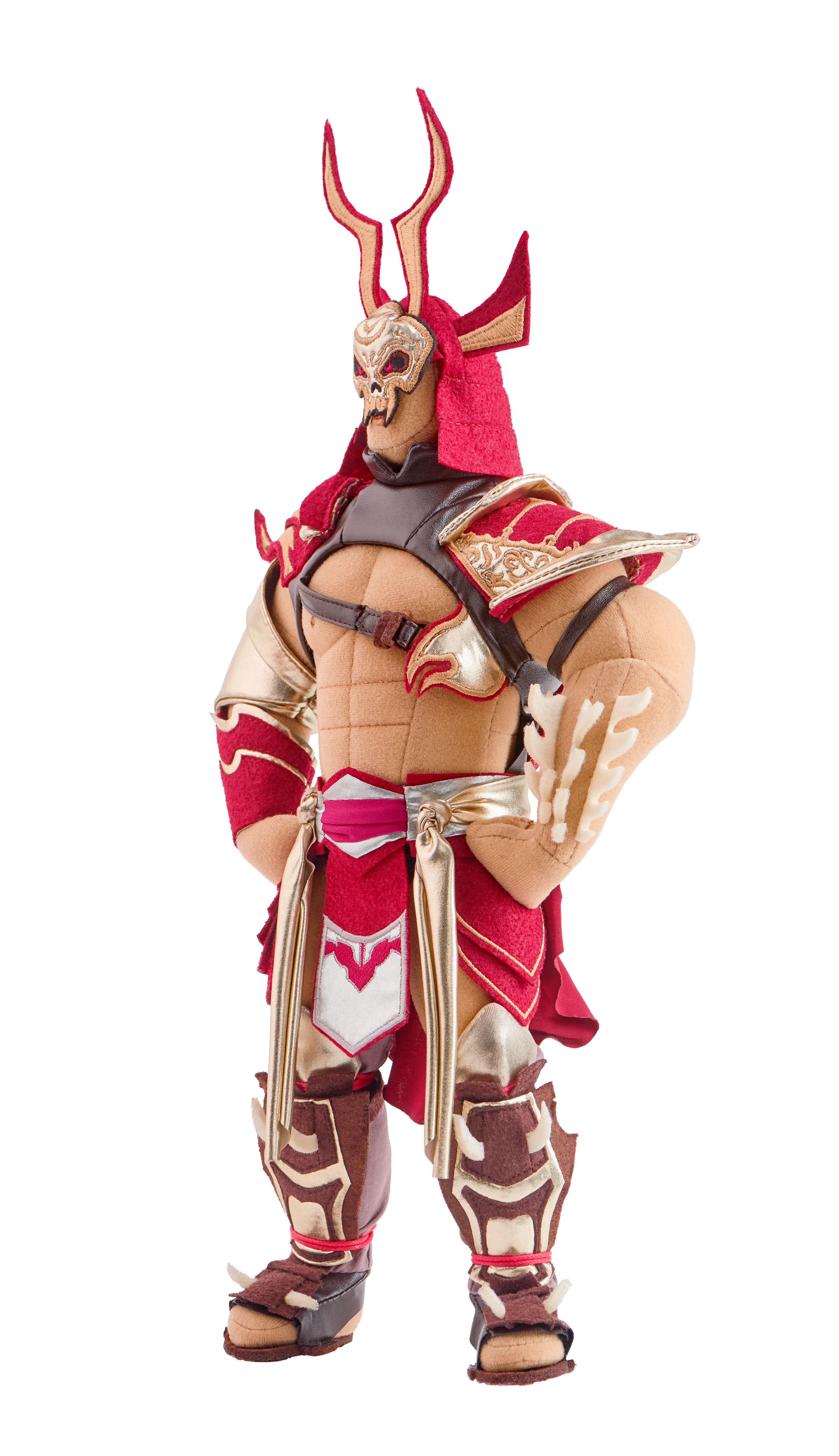 Eine Plüschkriegerpuppe mit rotem und goldenem Outfit, gehörntem Helm und einer schädelartigen Maske. Sie steht mit verschränkten Armen vor weißem Hintergrund.