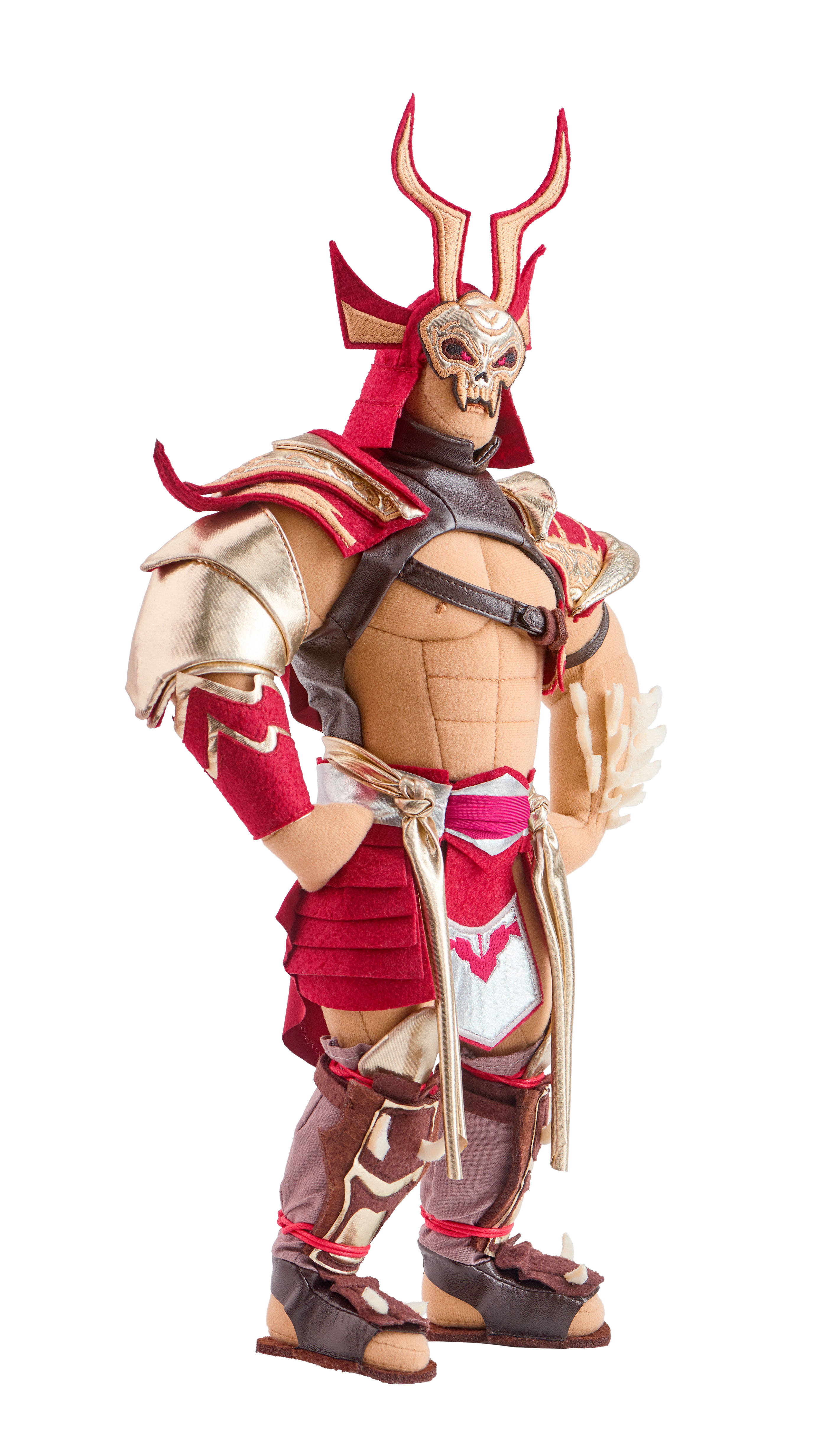 Eine Plüschkriegerpuppe mit roter und goldener Rüstung, einem gehörnten Helm und einer schädelartigen Maske. Sie steht mit verschränkten Armen auf weißem Hintergrund.