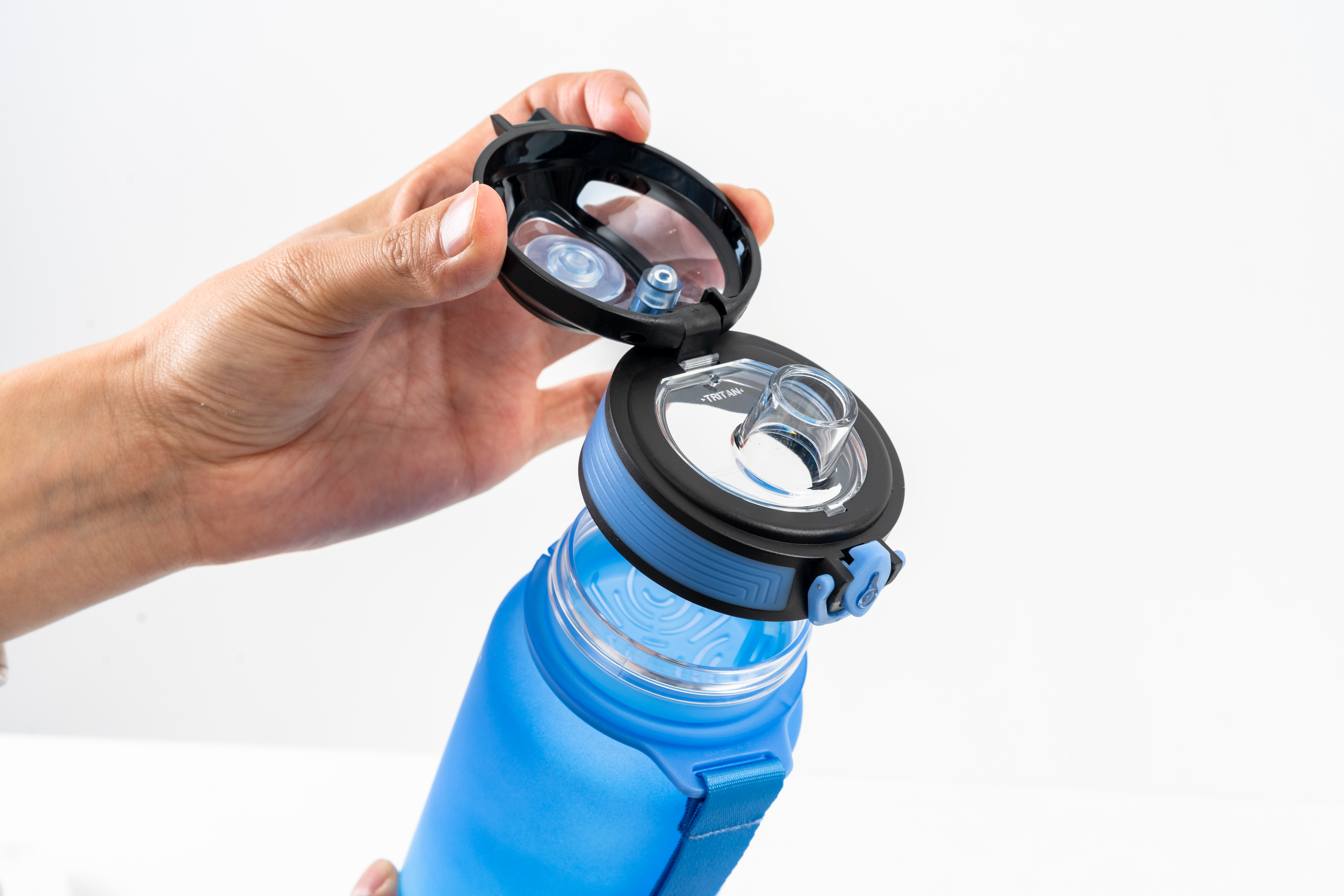 Een hand opent een blauwe waterfles. De fles is gedeeltelijk open, de binnenkant zichtbaar. Witte achtergrond.