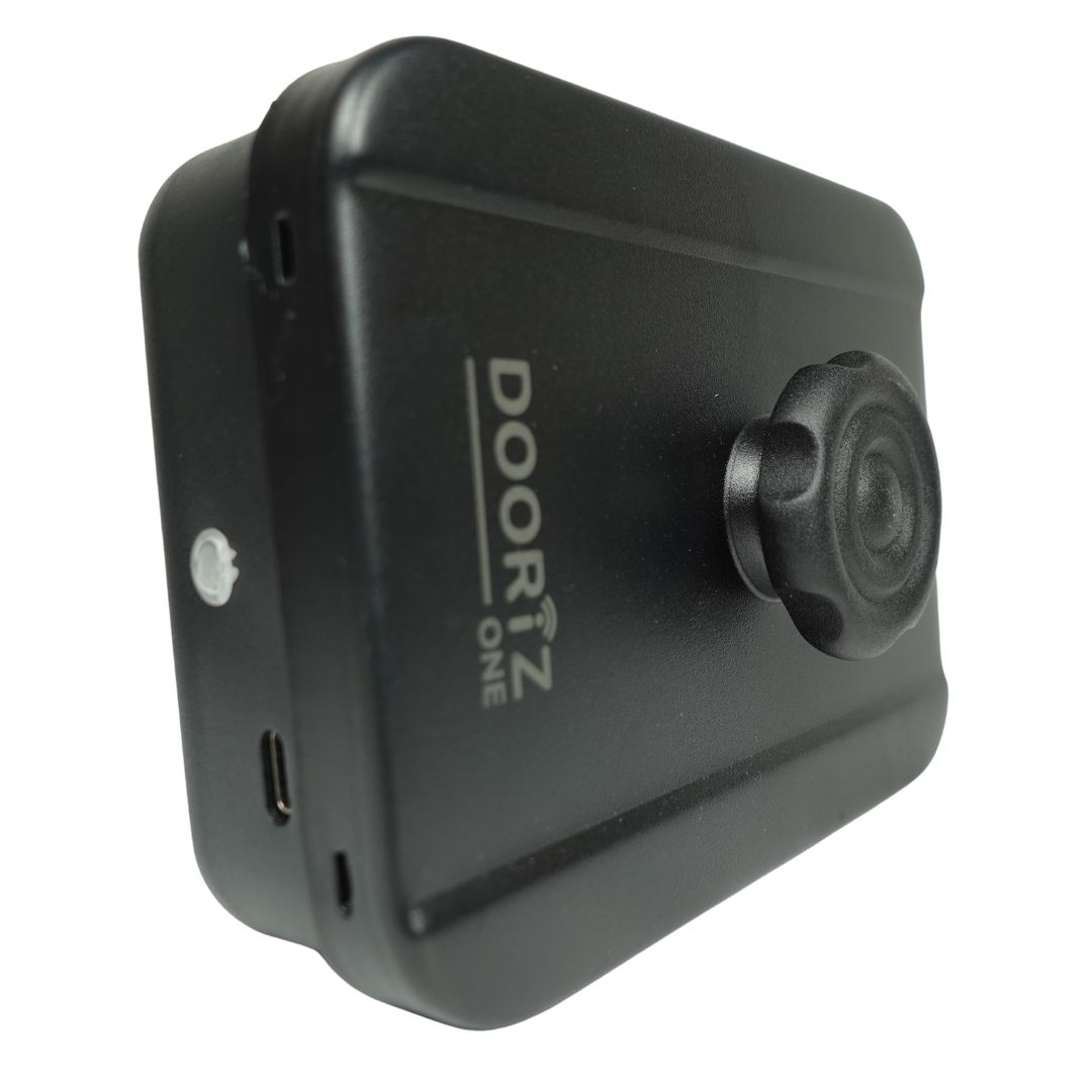 Se muestra un Smart Lock Dooriz One negro. Tiene una perilla a la derecha y un puerto de carga en la parte inferior. El fondo es blanco.