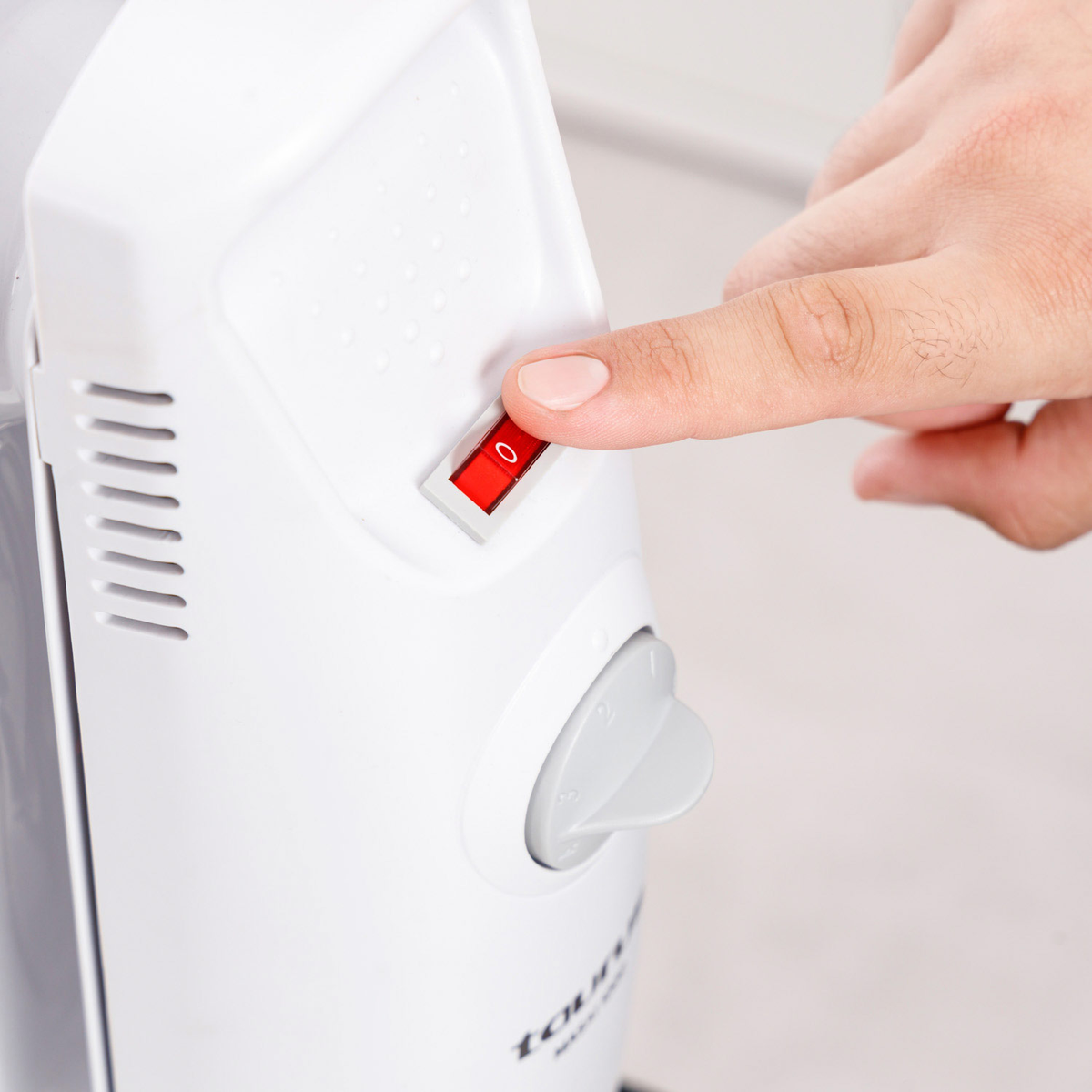 Ręka naciska czerwony włącznik zasilania na białym urządzeniu. Przełącznik jest w pozycji wyłączonej. Szare pokrętło jest widoczne pod przełącznikiem.