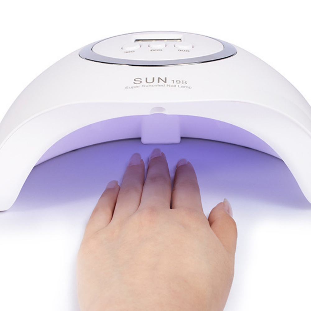 Eine Hand mit gepflegten Nägeln wird unter eine weiße UV-Nagellampe gelegt. Die Lampe ist an und strahlt violett.