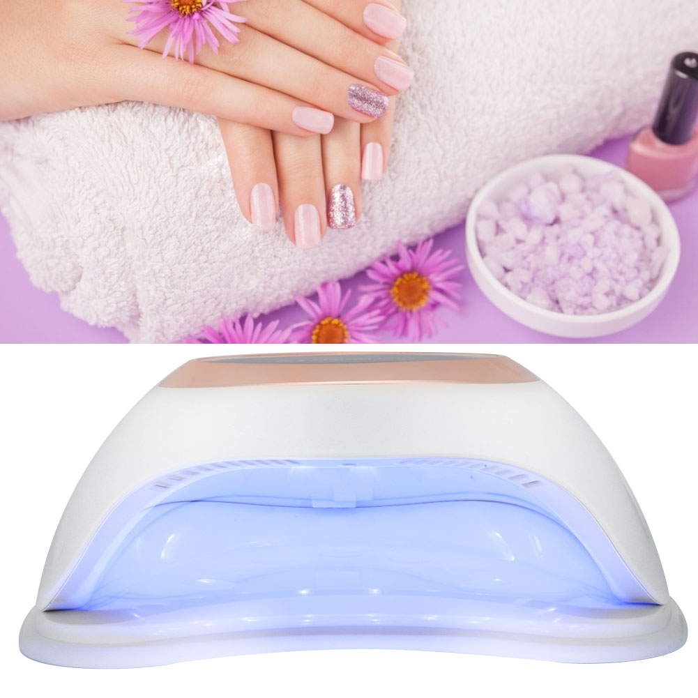 Hände mit manikürten rosa Nägeln, Handtuch, Blumen, Nagellack und einer Nagellampe. Der Hintergrund ist lila.