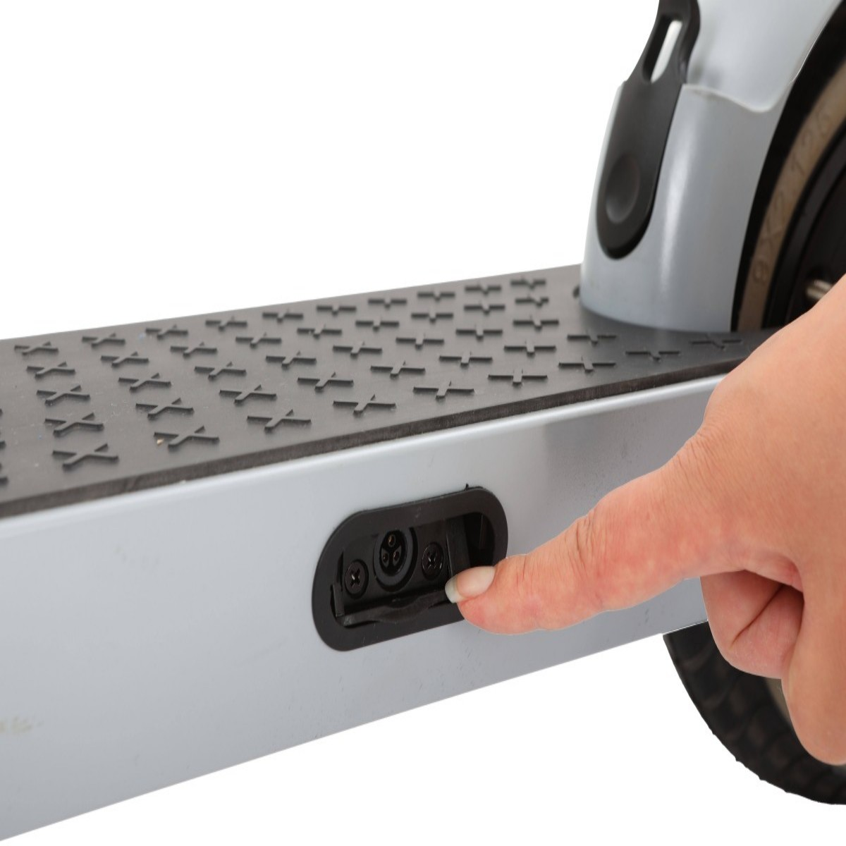 Dłoń dotyka portu ładowania szarej hulajnogi elektrycznej. Hulajnoga ma czarną, teksturowaną powierzchnię i czarne koło.