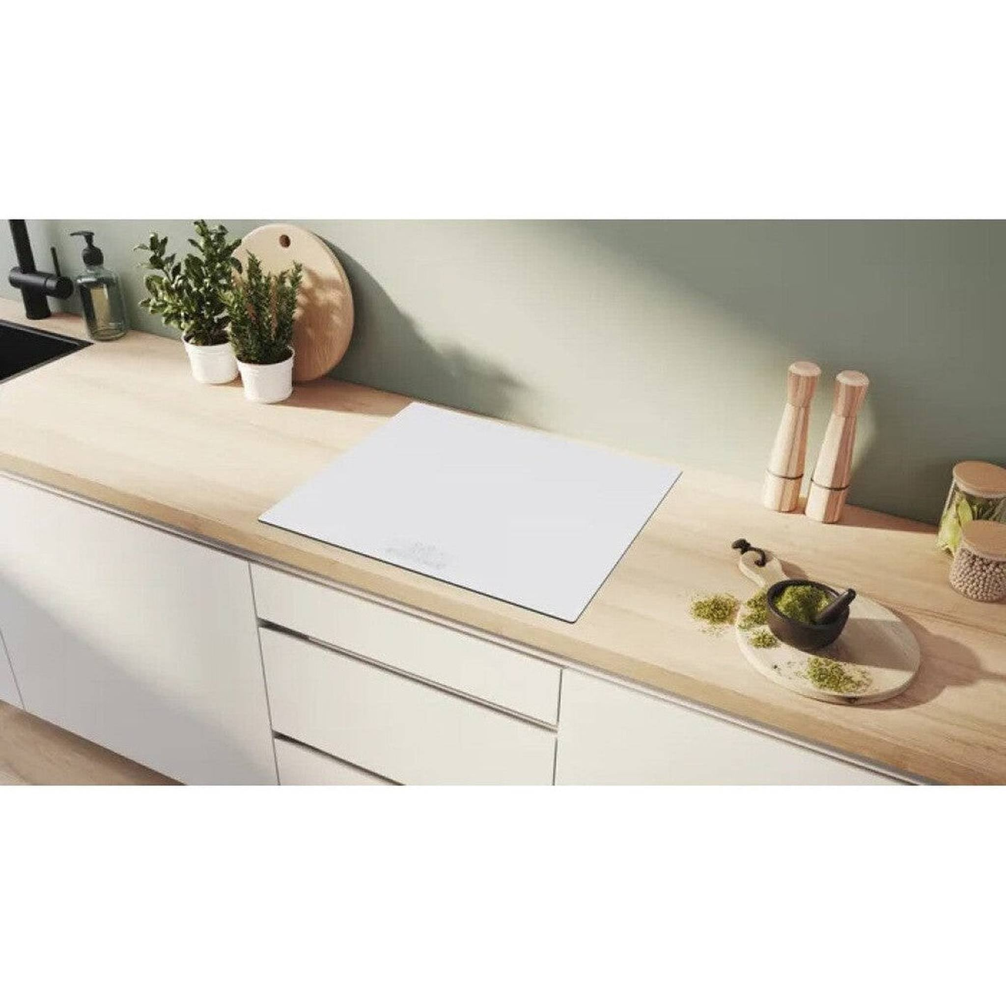 Blat kuchenny z białą płytą grzewczą, roślinami i drewnianymi akcesoriami. Moździerz i tłuczek na desce.