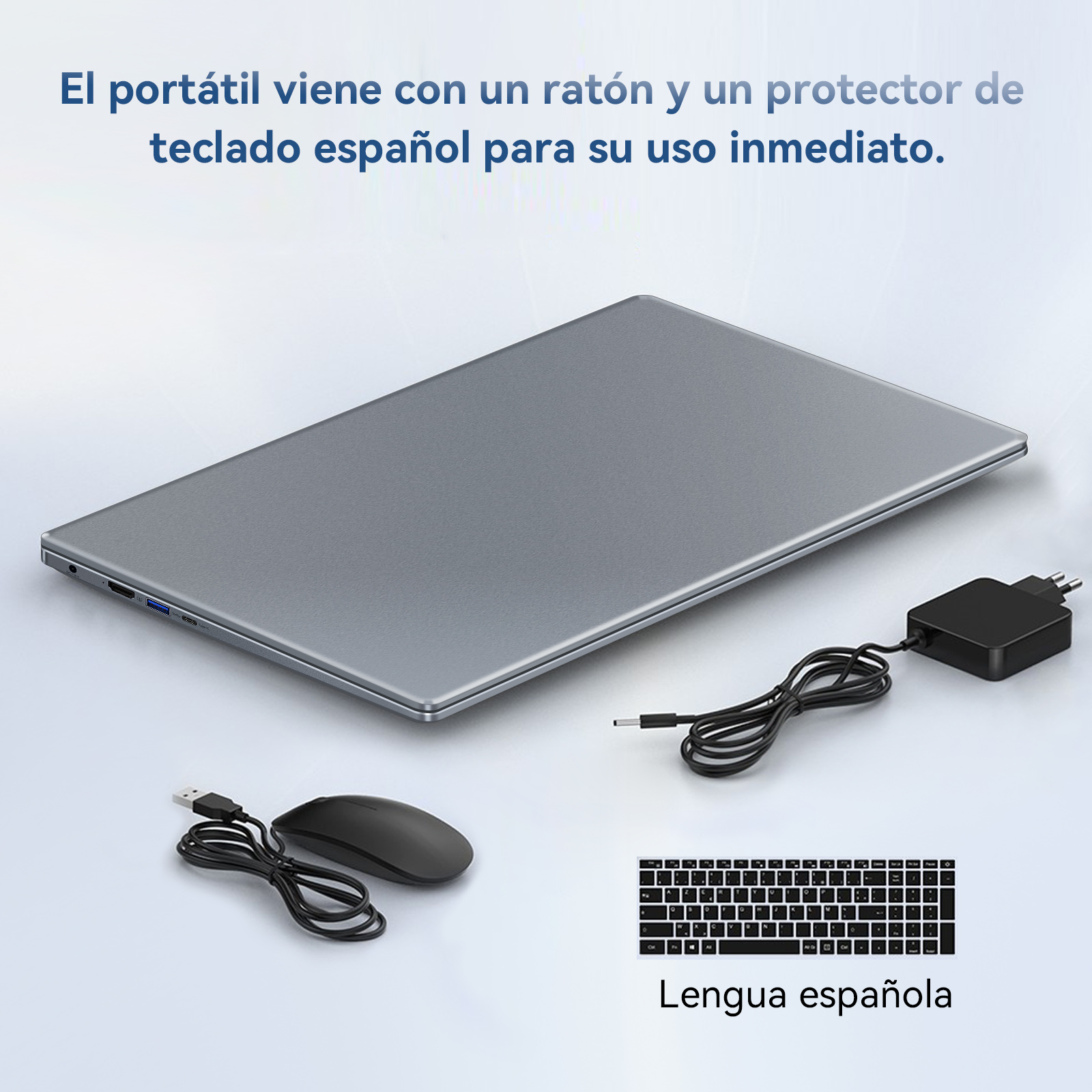 Un portátil con ratón, protector de teclado español y cargador, sobre una superficie blanca.