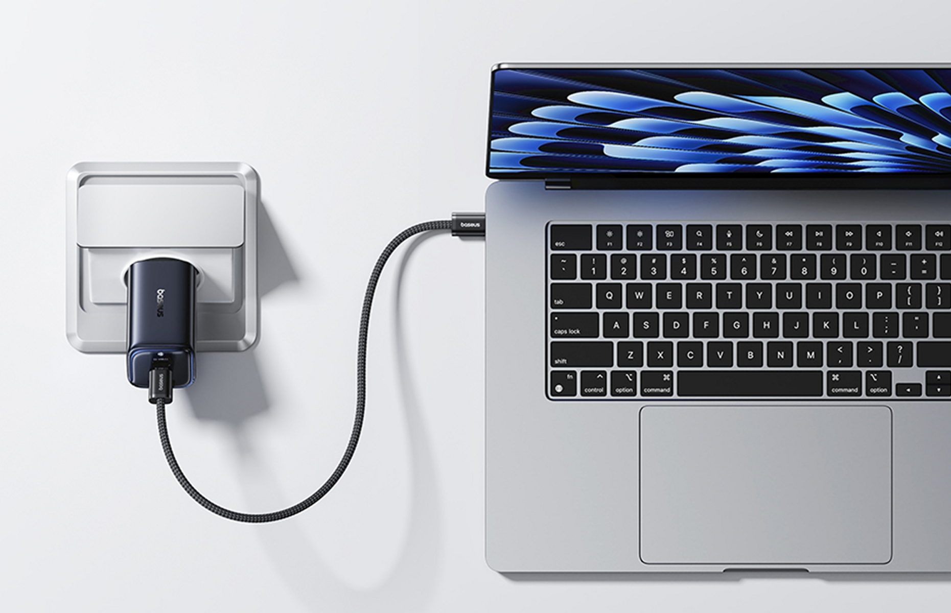Een laptop wordt opgeladen via een USB-C-kabel die is aangesloten op een wandcontactdoosadapter. De laptop staat op een wit oppervlak.
