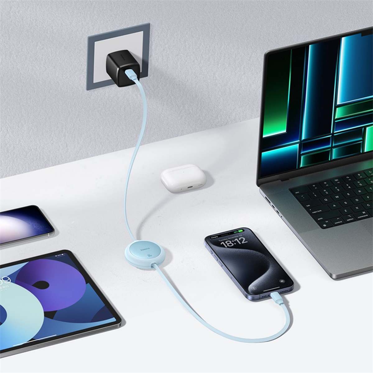 Ein Laptop, ein Telefon und ein Tablet werden aufgeladen. Ein Ladegerät ist an der Wand eingesteckt. AirPods liegen auf einer weißen Oberfläche.