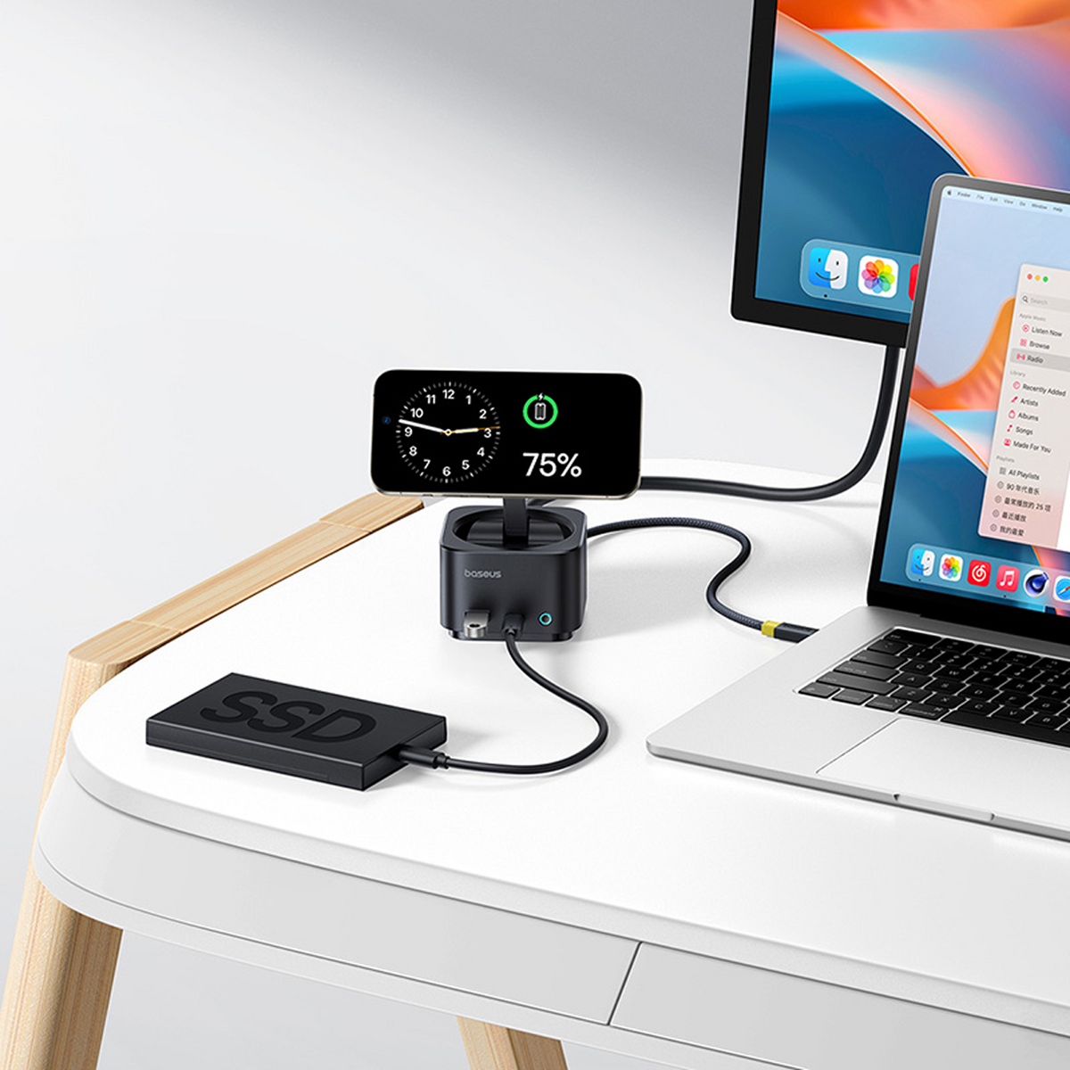 Ein Schreibtisch-Setup mit ladendem Telefon, SSD, Laptop und Monitor. Das Telefon zeigt Uhr und 75% Akku. Der Laptop zeigt eine Musik-App.