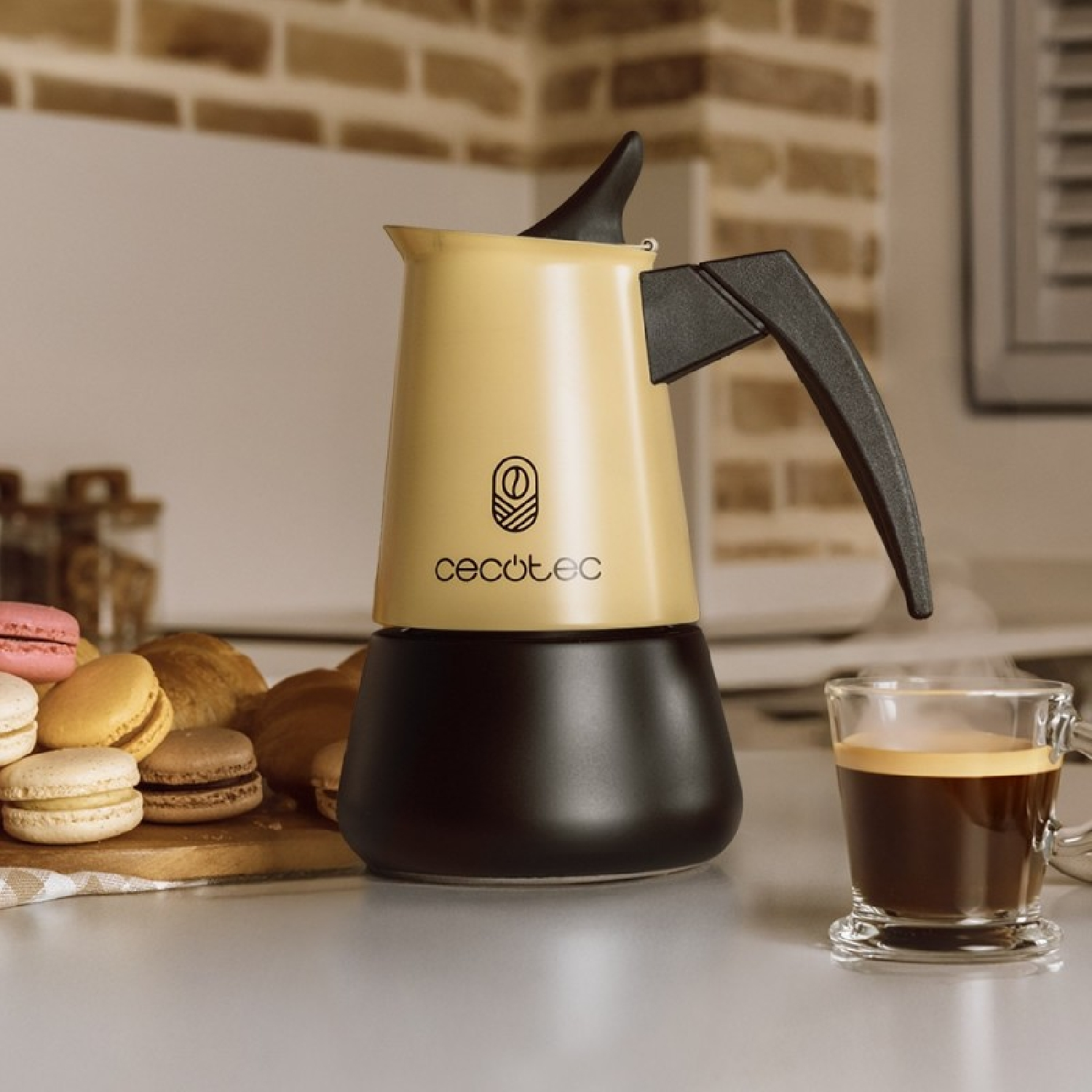 Una caffettiera gialla e nera con una tazza di caffè e pasticcini su un tavolo. Parete di mattoni sullo sfondo.