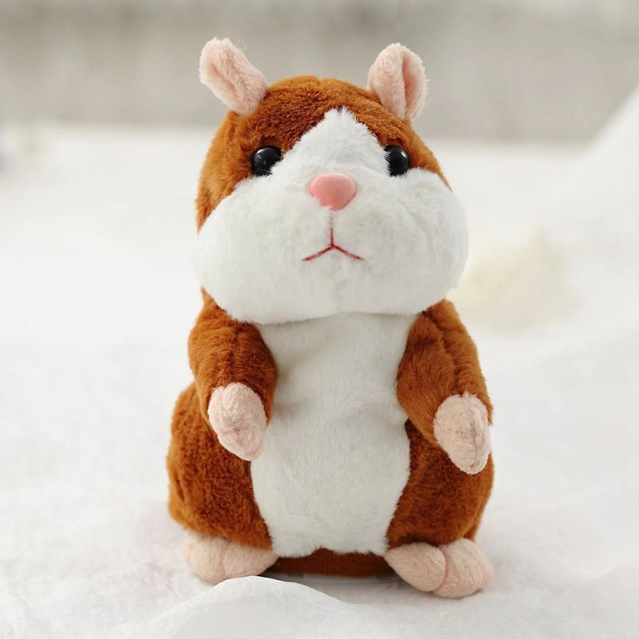 Ein Plüschhamster-Spielzeug mit braunem und weißem Fell, rosa Nase und Ohren, steht auf einer weißen Oberfläche.