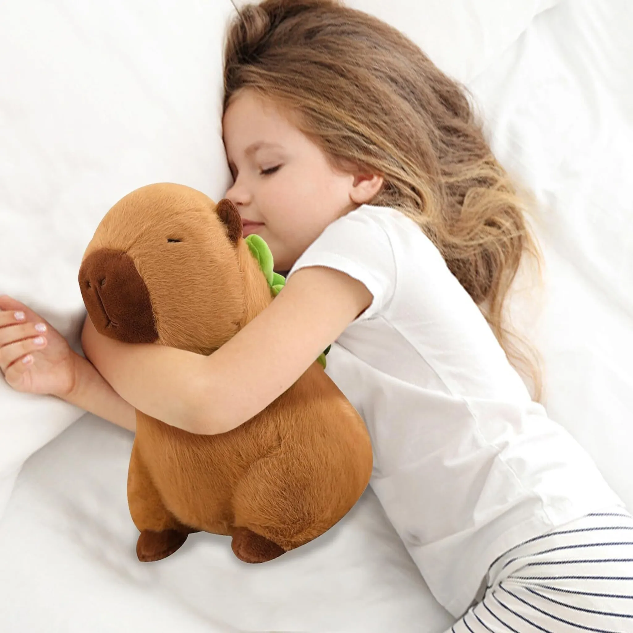 Ein schlafendes Mädchen umarmt ein Capybara-Plüschtier auf einem weißen Bett. Das Plüschtier ist braun, das Mädchen trägt Weiß und hat langes Haar.