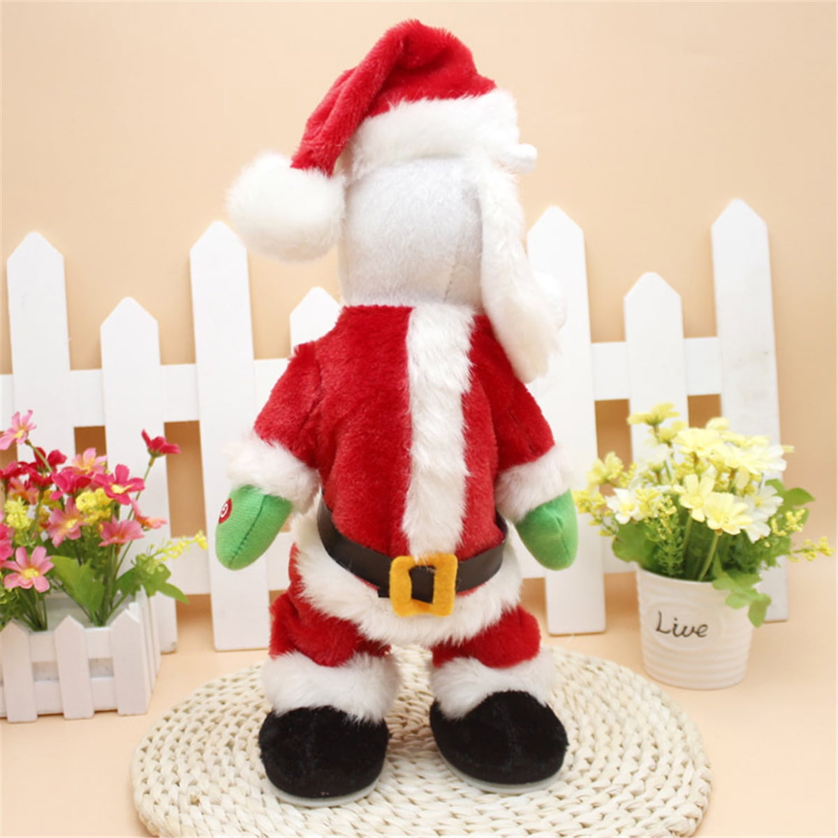 Eine Weihnachtsmannpuppe, die einen roten Anzug und Hut trägt, steht auf einer gewebten Matte. Weißer Zaun und Blumen sind im Hintergrund.