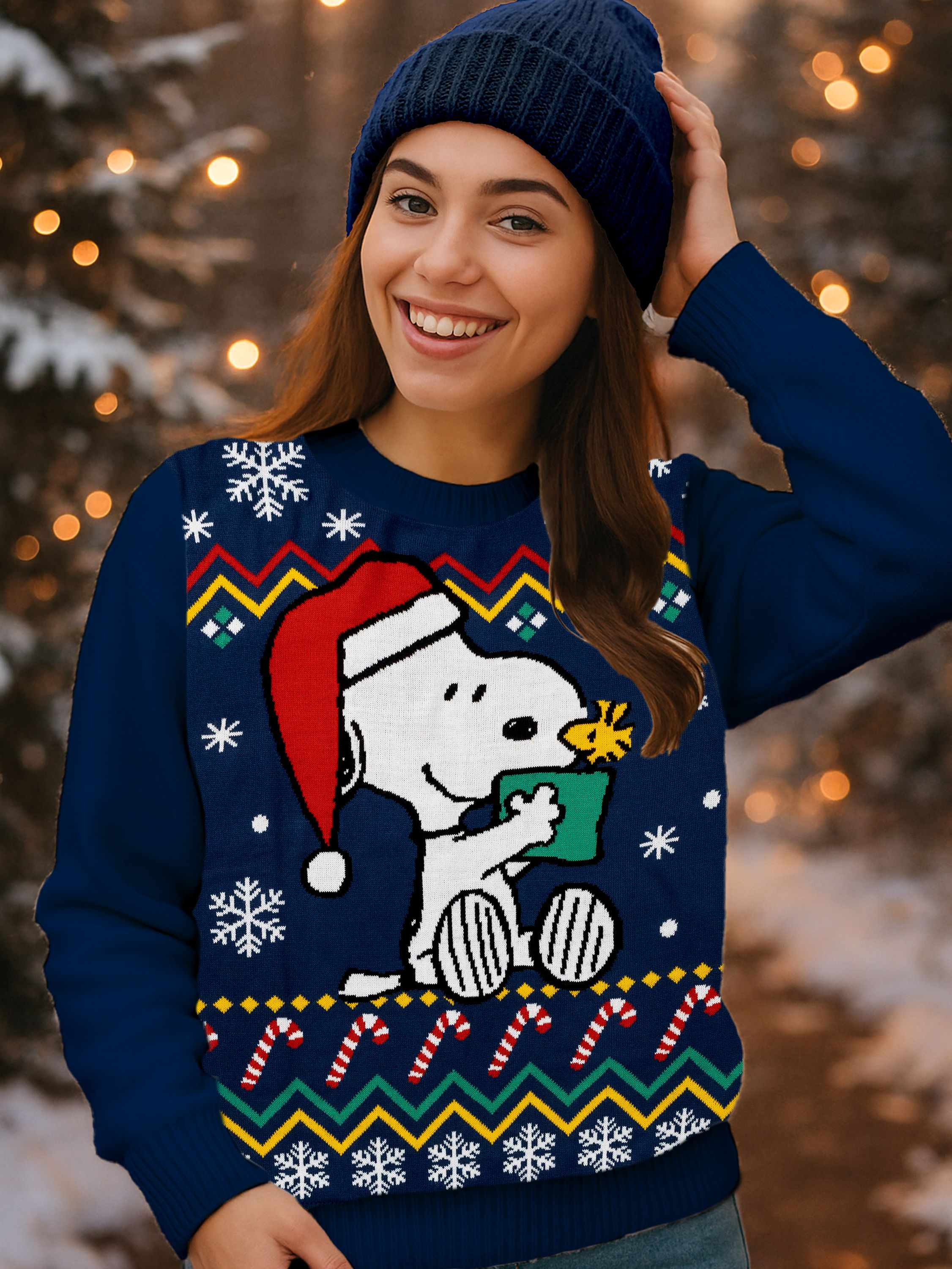 Frau mit blauer Mütze und Snoopy-Pullover lächelt. Der Hintergrund zeigt unscharfe Lichter und Bäume.