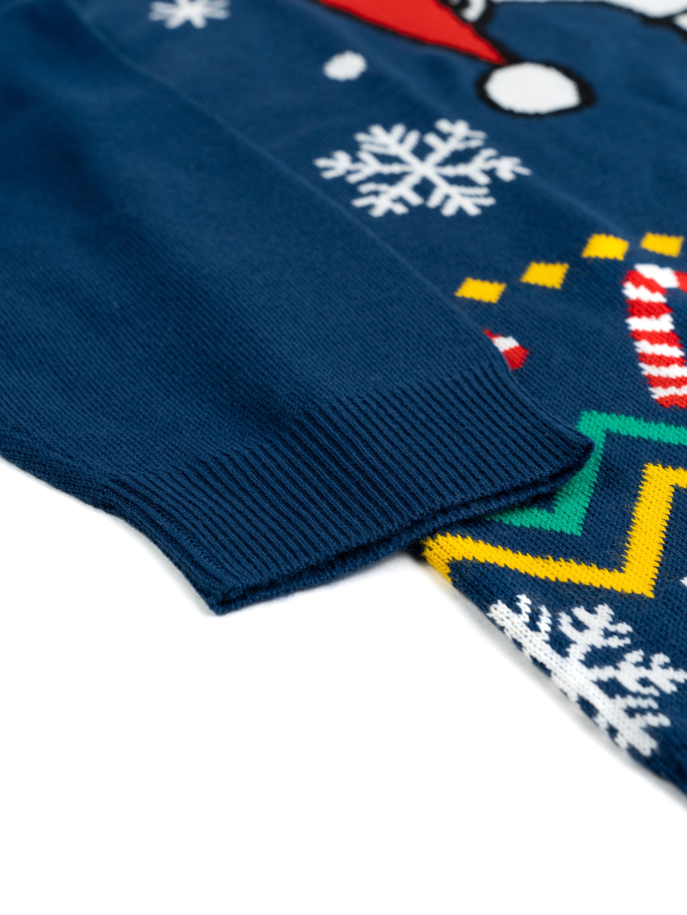 Nahaufnahme eines blauen Weihnachtspulloverärmels, Schneeflocken- und Zuckerstangenmuster auf dem Stoff. Weißer Hintergrund.